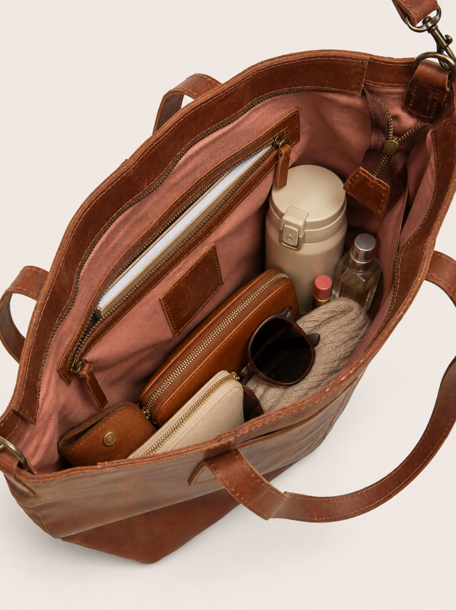 Filled interior shot of a whiskey tote bag with a water bottle, wallet, glasses, pouches, sweater and more with an interior zipper with a notebook inside. #Color_Whiskey