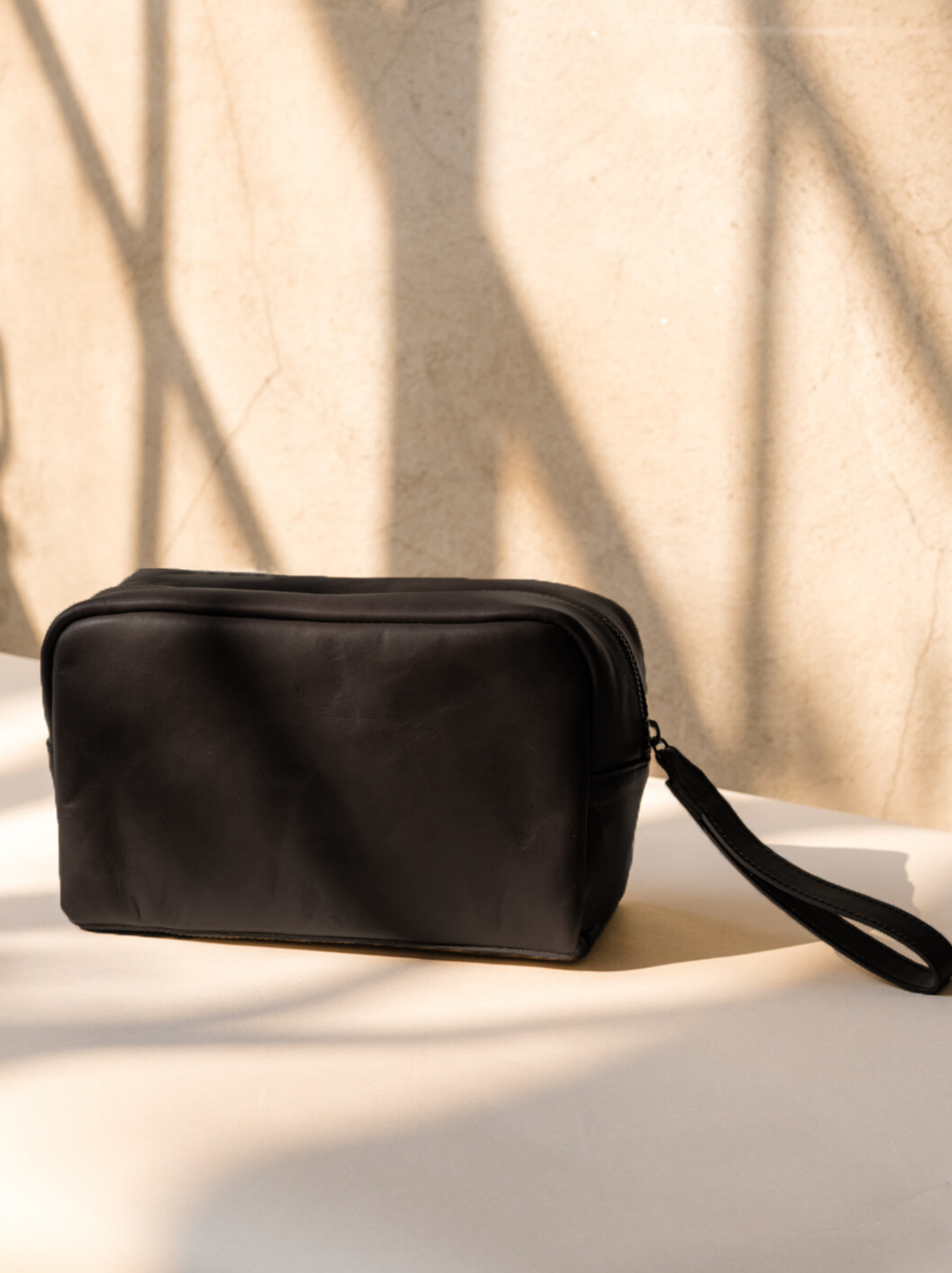 Side of black leather dopp kit on a light background with leather hang strap. #Color_Black