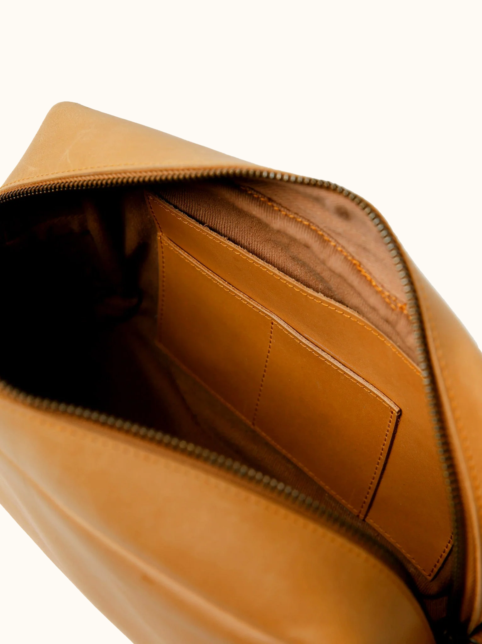 Interior pocket of leather dopp kit on white background. #Color_Cognac