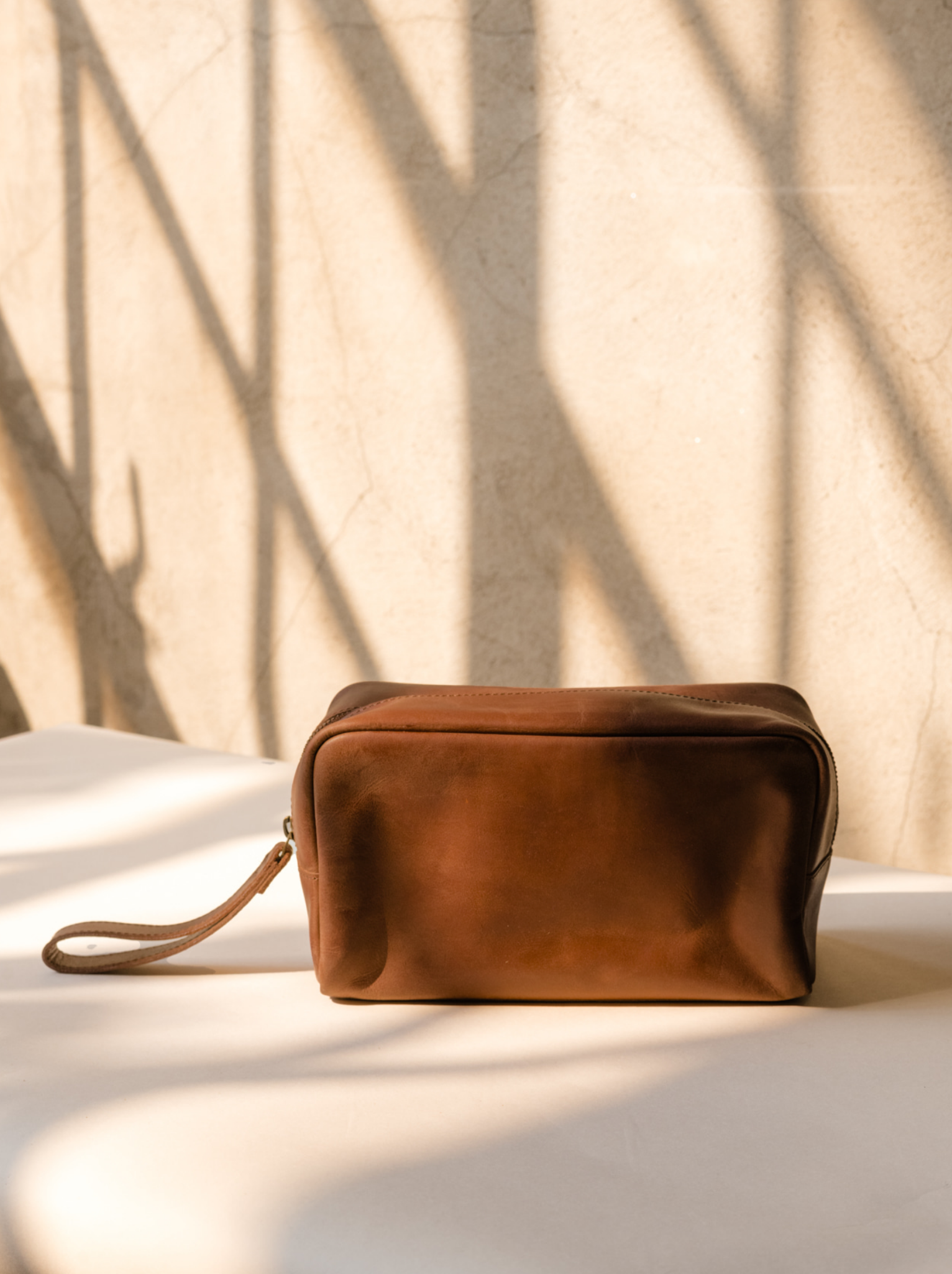 Side profile of brown leather dopp kit on a light background. #Color_Whiskey