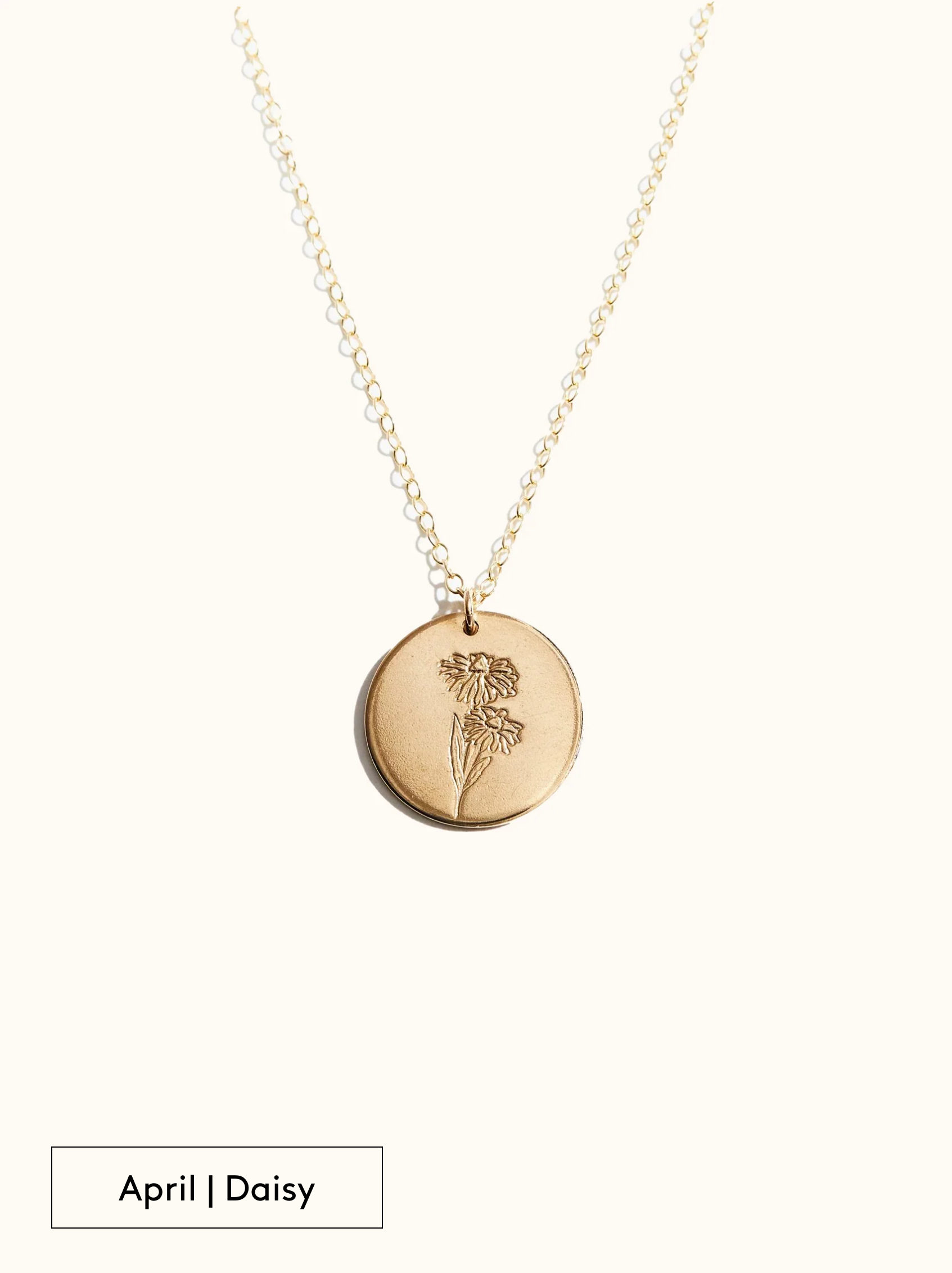 A gold-filled necklace with a round tag pendant featuring an engraved Daisy, noted as April's birth month flower, attached to a 24 inch chain on a neutral background.