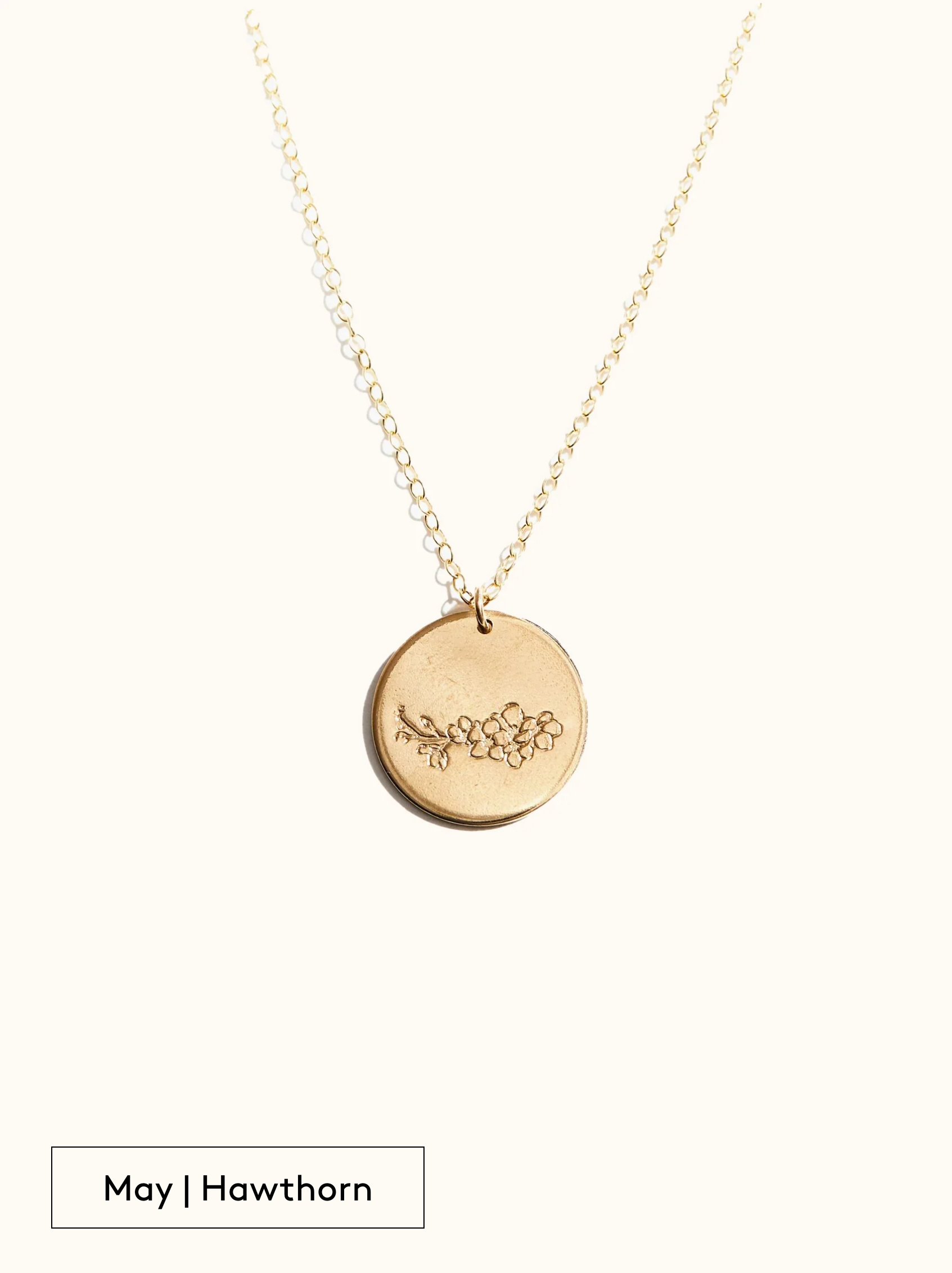 A gold-filled necklace with a round tag pendant featuring an engraved Hawthorn, noted as May's birth month flower, attached to a 24 inch chain on a neutral background.
