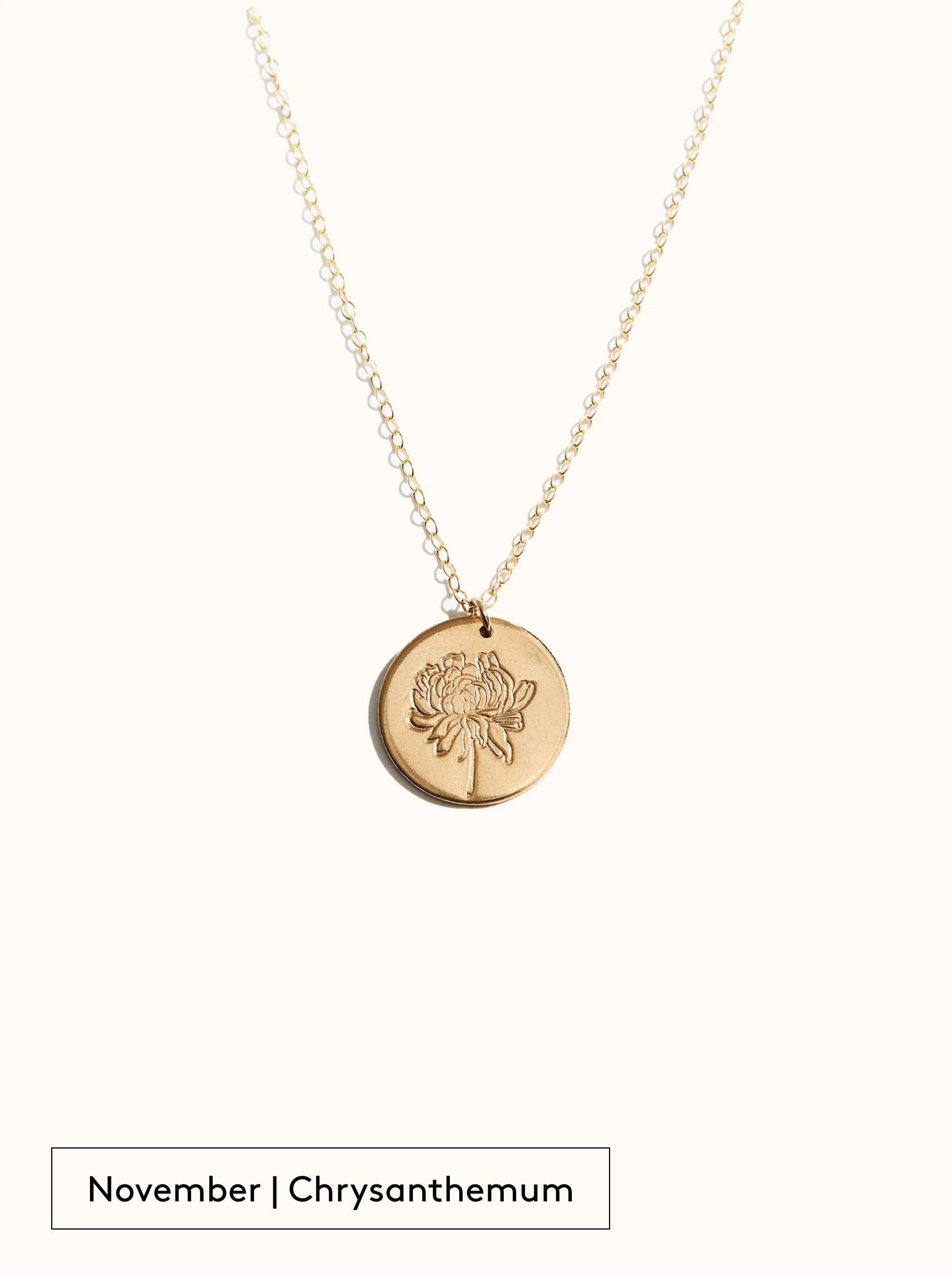 A gold-filled necklace with a round tag pendant featuring an engraved Chrysanthemum, noted as November's birth month flower, attached to a 24 inch chain on a neutral background.