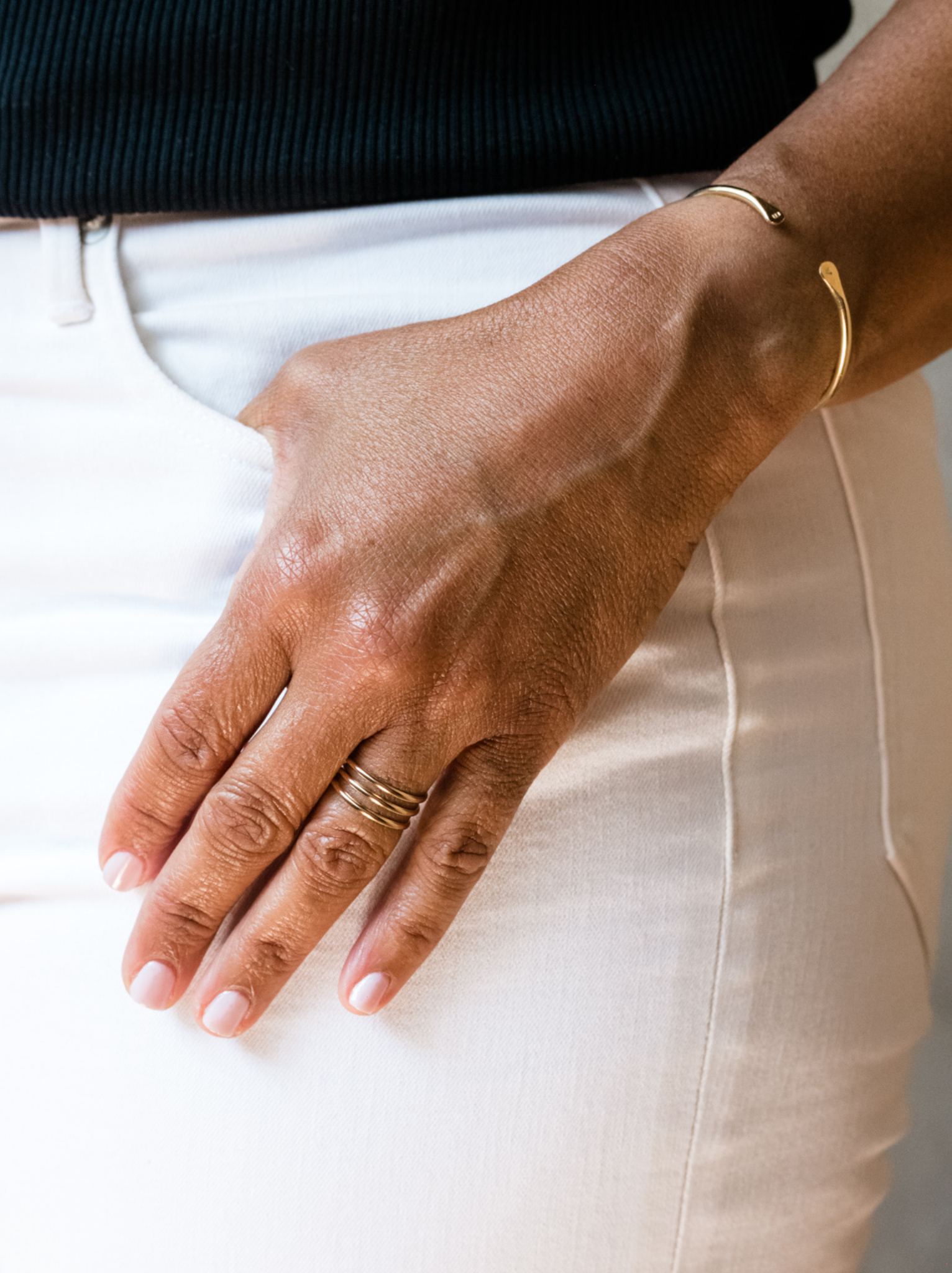 Close up of woman wearing a gold three spiral ring on her left ring finger with cuff bracelet.