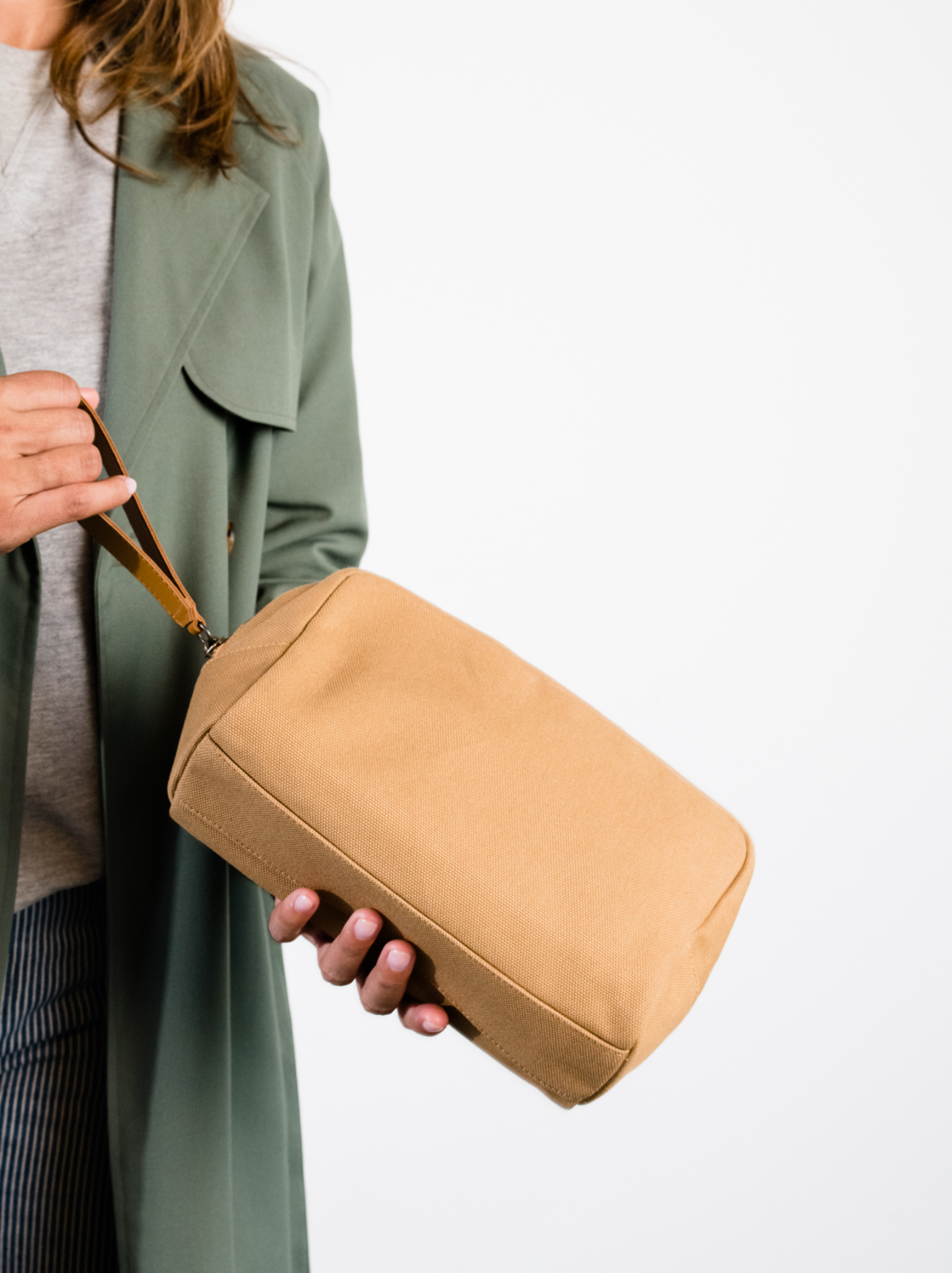 Woman holding a tan canvas dopp kit against a white background
