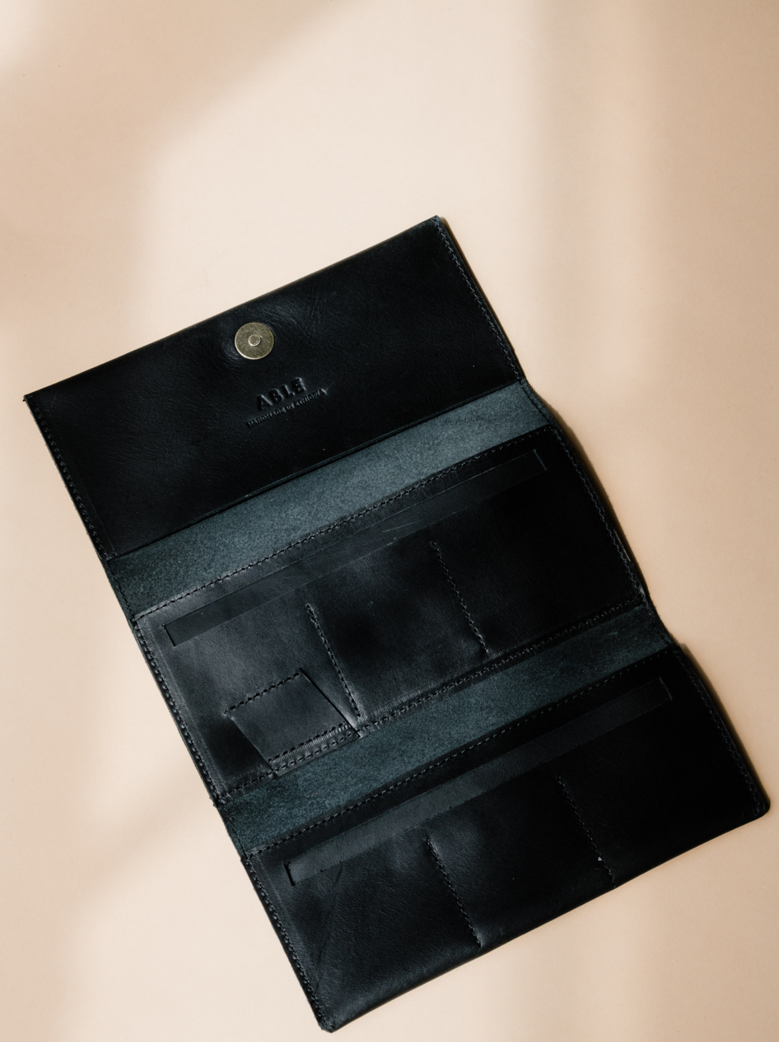 Opened trifold black leather wallet with card slots and pen holder with magnetic closure on neutral background. #Color_Black