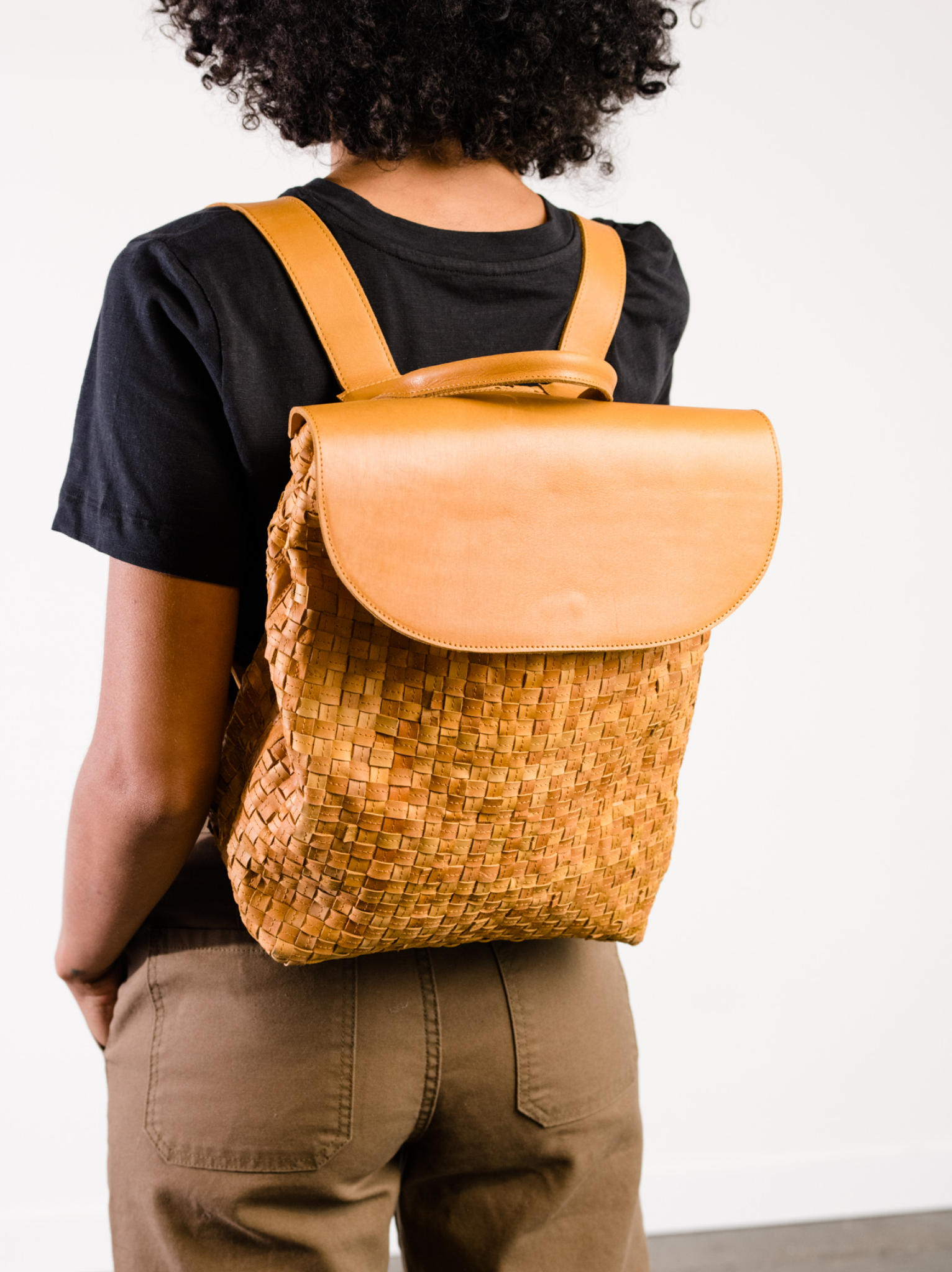 Woman wearing a basketweave orange cognac leather backpack with solid leather flap closure on her back. #Color_Cognac