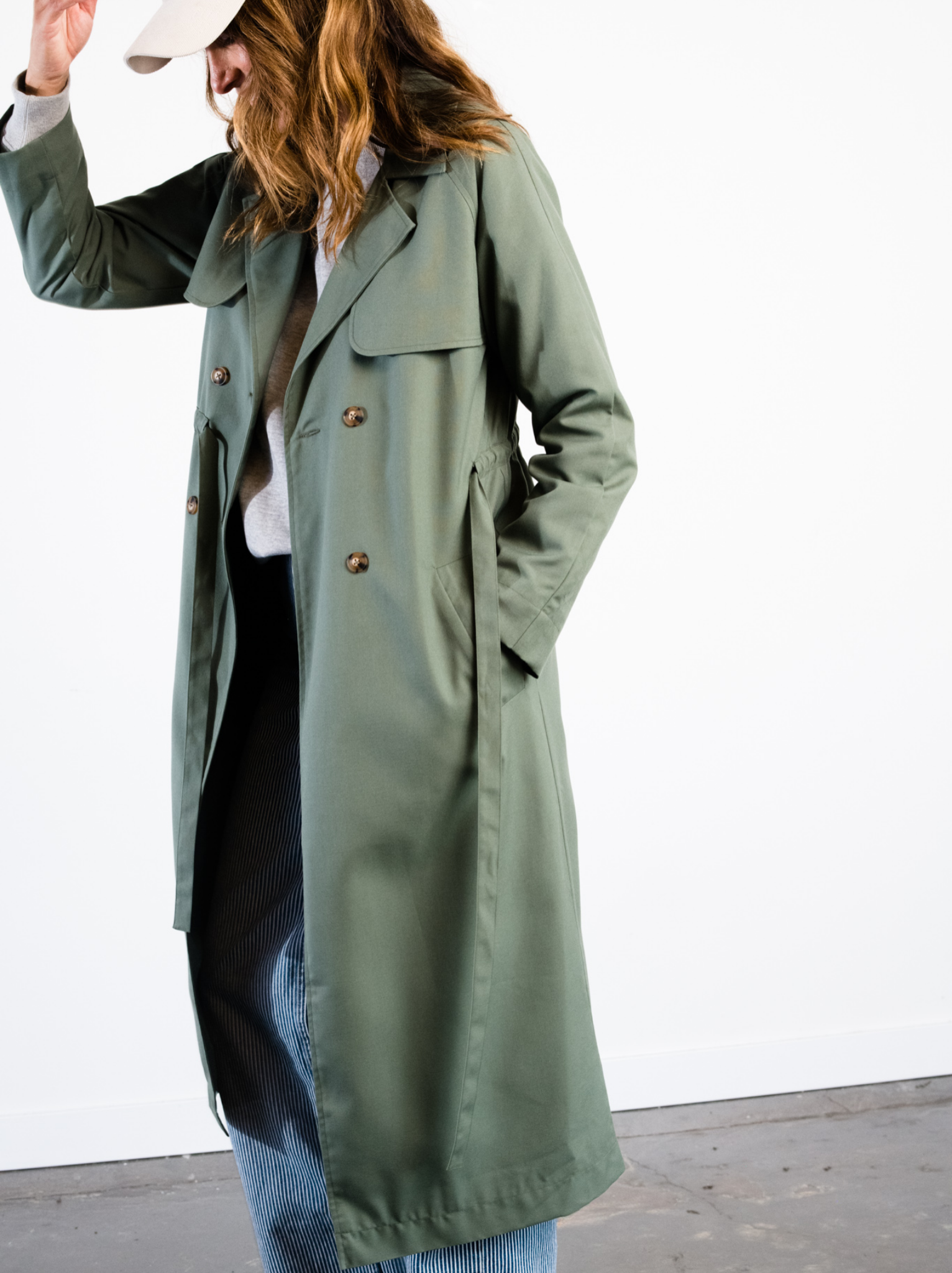 Side profile of woman wearing an unbelted green trench coat with hand in pocket. #Color_Moss