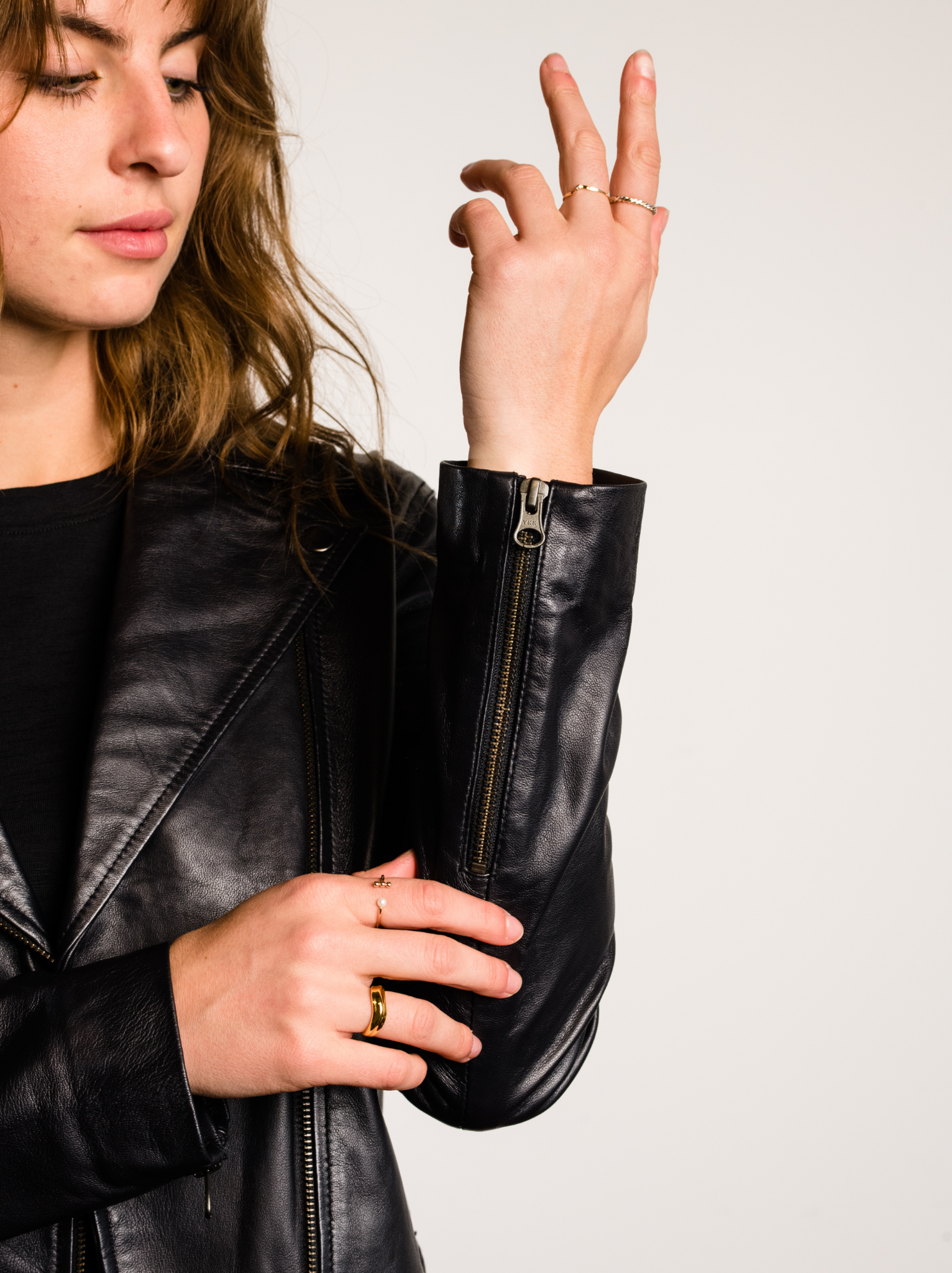 A woman showing the zipper detail of the sleeve of a black leather jacket. #Color_Black