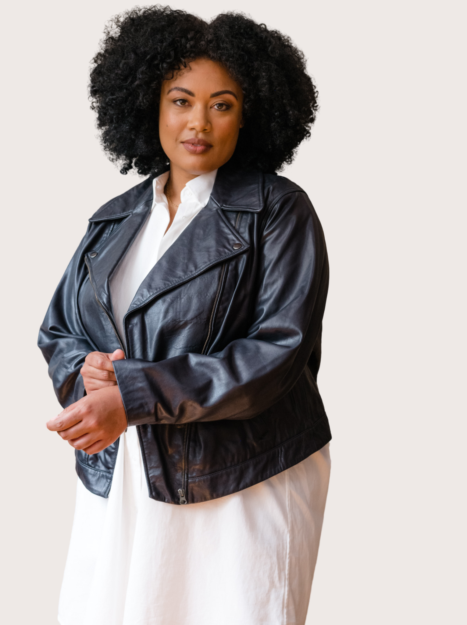 A woman wearing a black leather jacket with a white shirt dress against white wall. #Color_Black