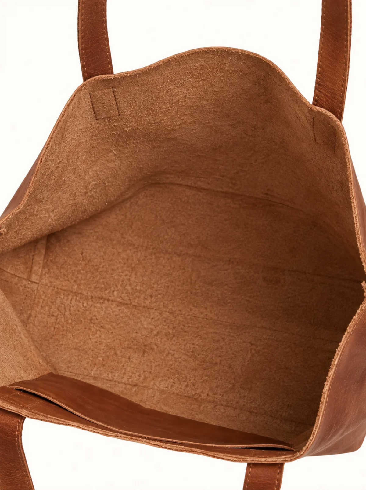 Close-up of the interior of a brown leather tote bag, showing the tan-brown suede and the brown leather handles against a white background. #Color_Camel