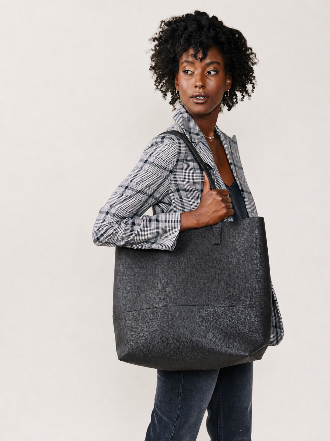 Woman holding a black pebbled textured tote bag, wearing a blazer, against a white background. #Color_Pebbled Black