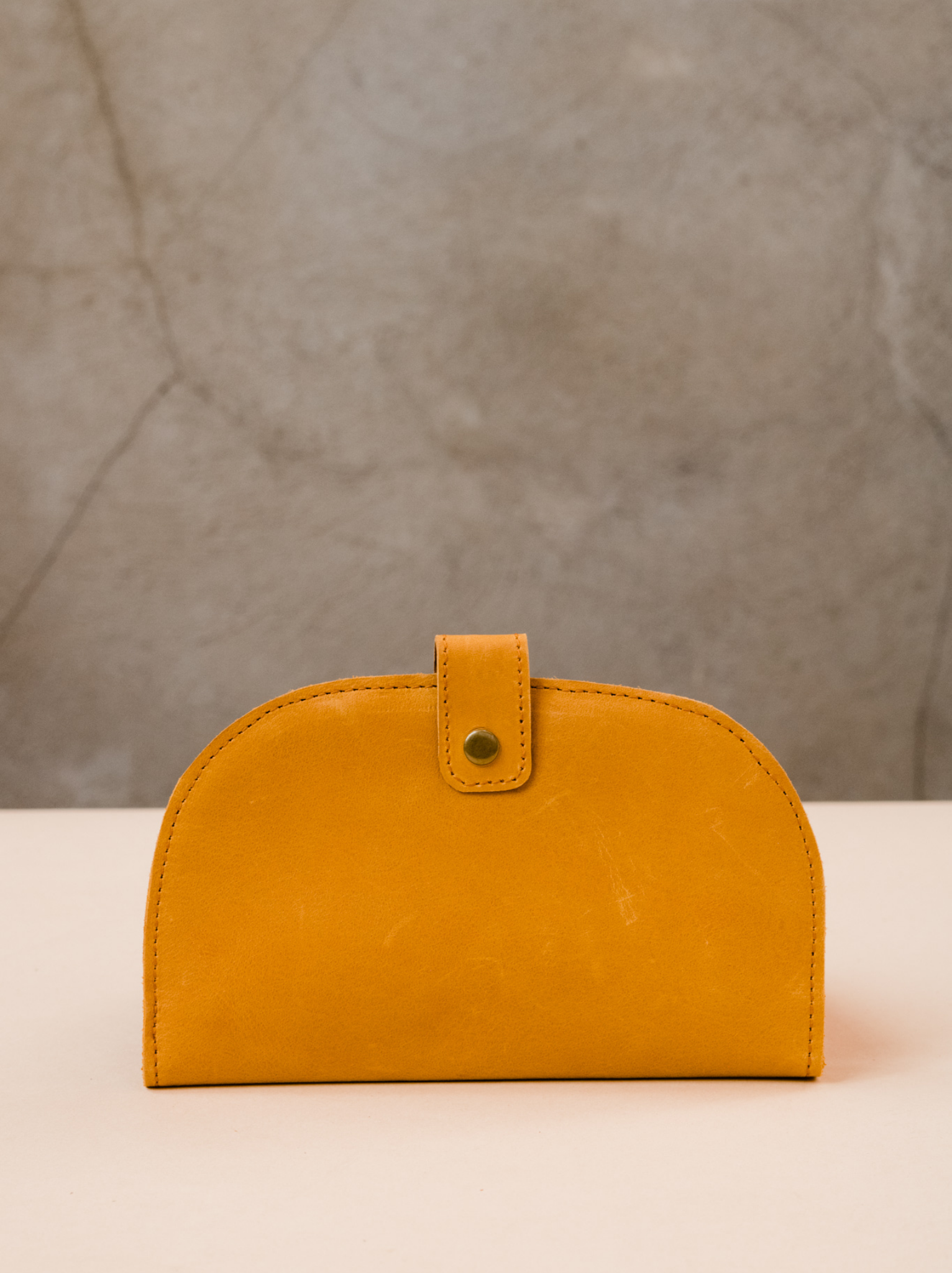 Cognac orange leather wallet with top snap closure on tan surface against neutral background. #Color_Cognac