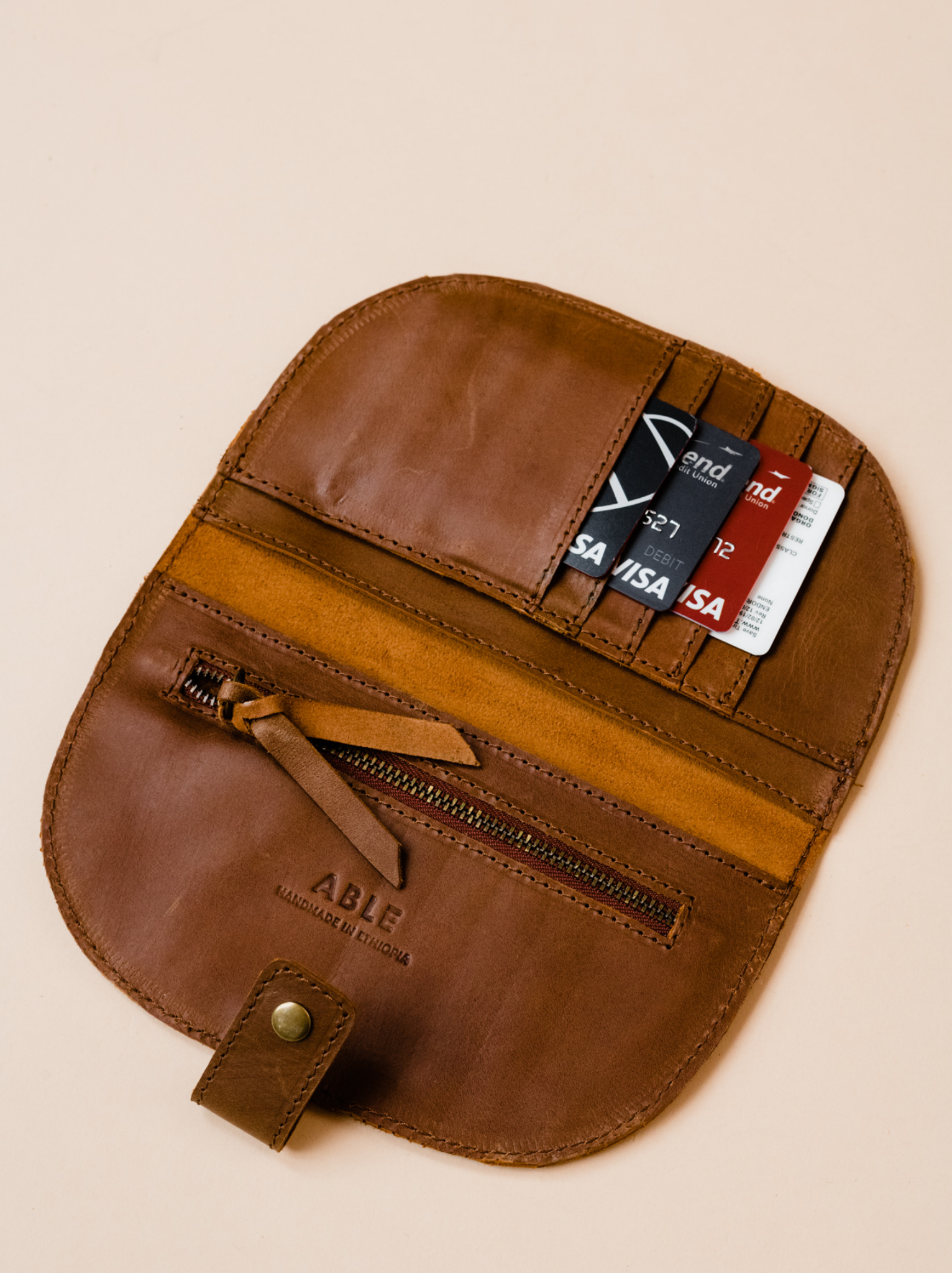 Interior of brown leather wallet with cards in card slots with a zipper pocket and debossed brand logo on a neutral background. #Color_Whiskey