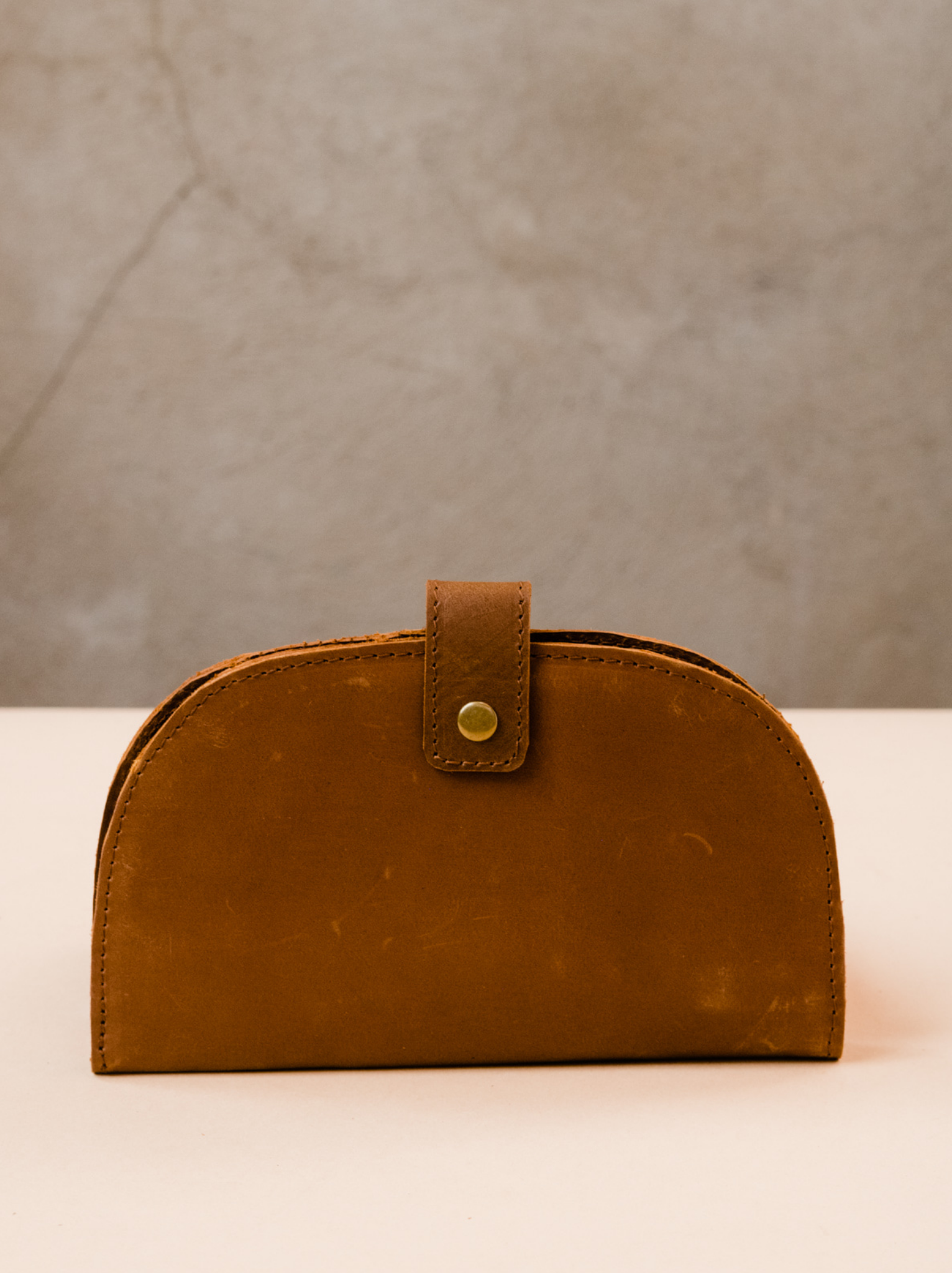 Brown leather wallet with top gold snap closure on tan surface against neutral background. #Color_Whiskey