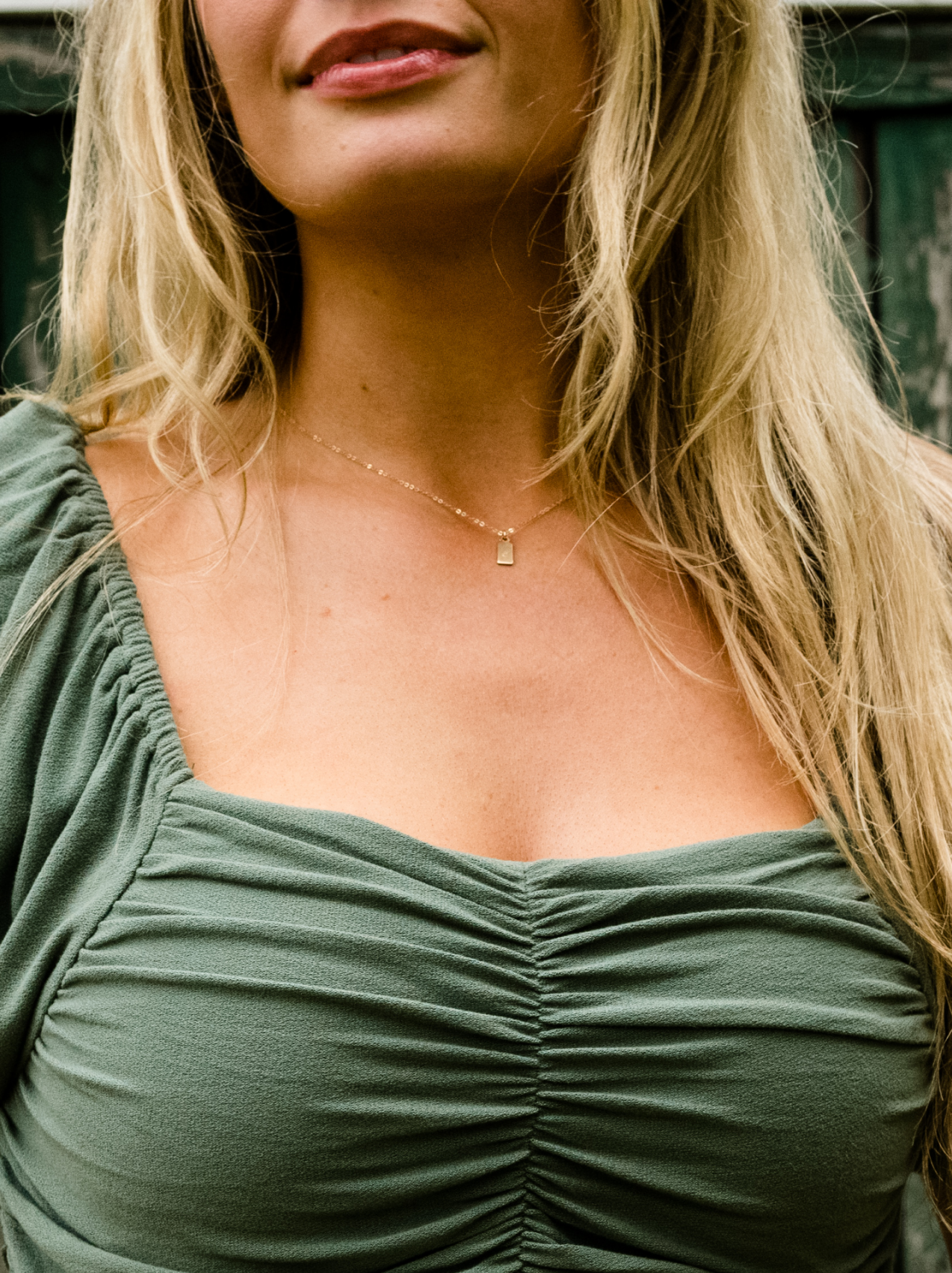 A woman wearing a gold necklace a mini dog tag pendant.