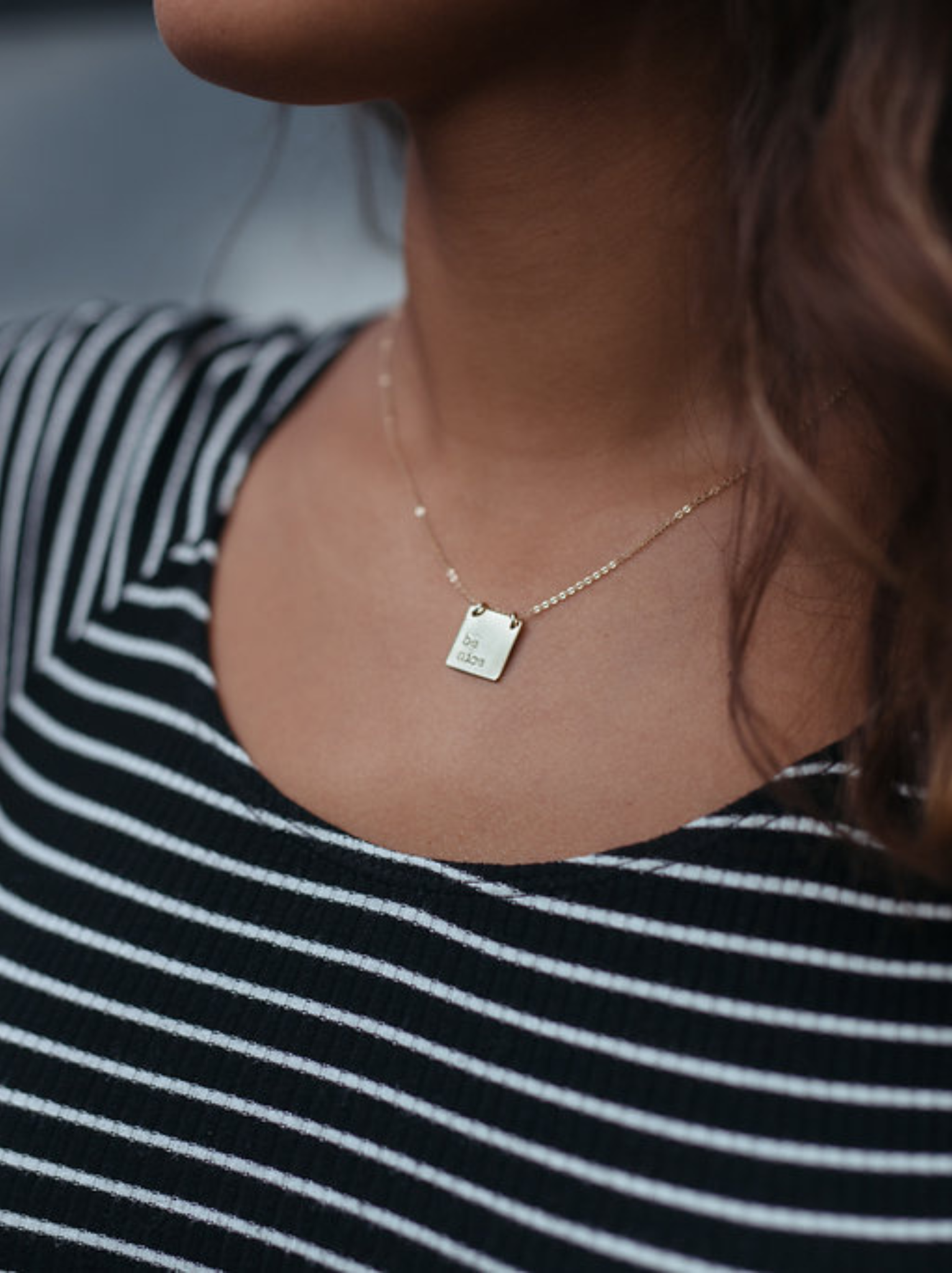 Close up of a woman wearing a gold necklace with a personalized square pendant.
