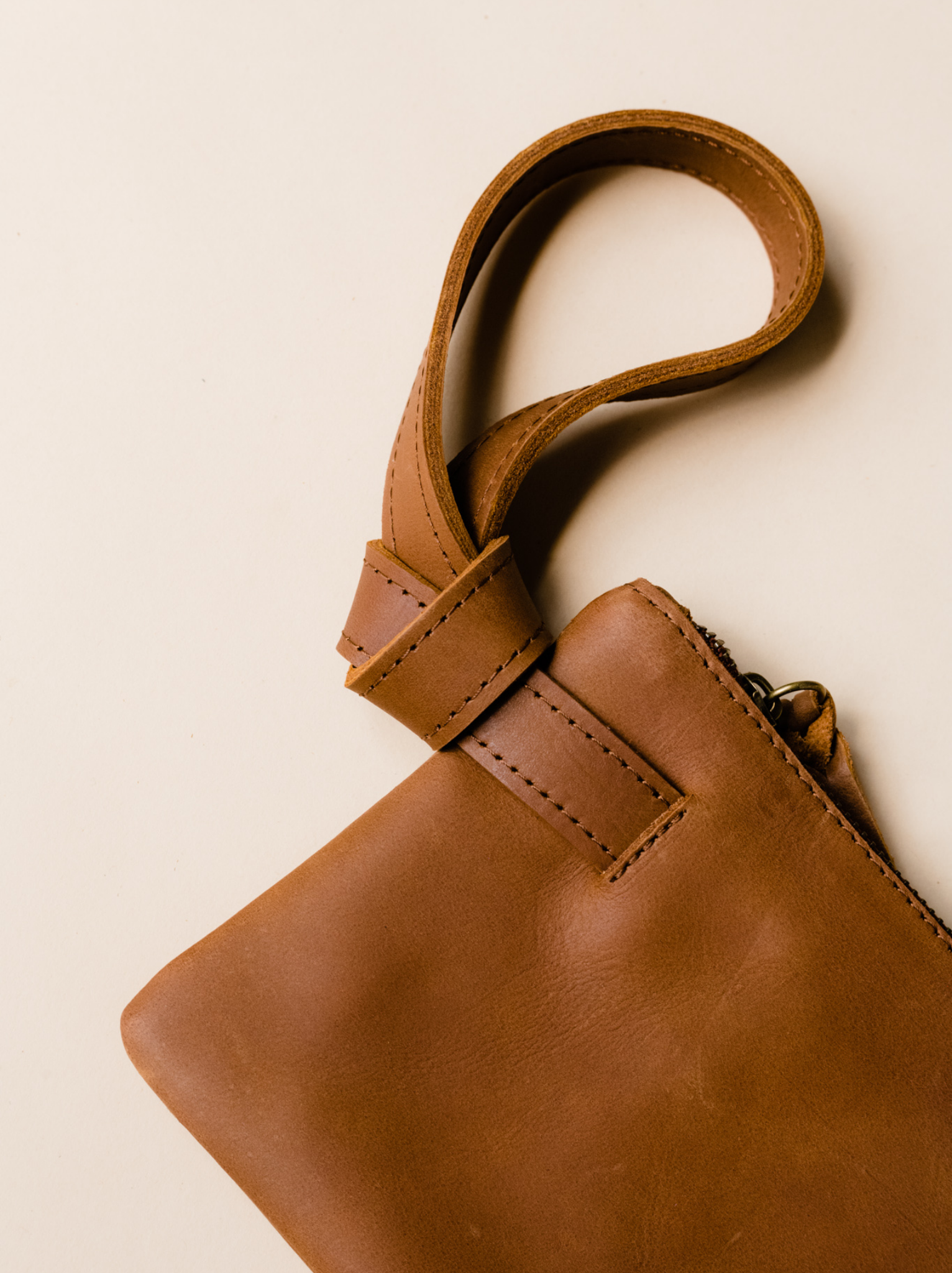 Knotted brown leather wristlet handle detail on neutral background. #Color_Whiskey