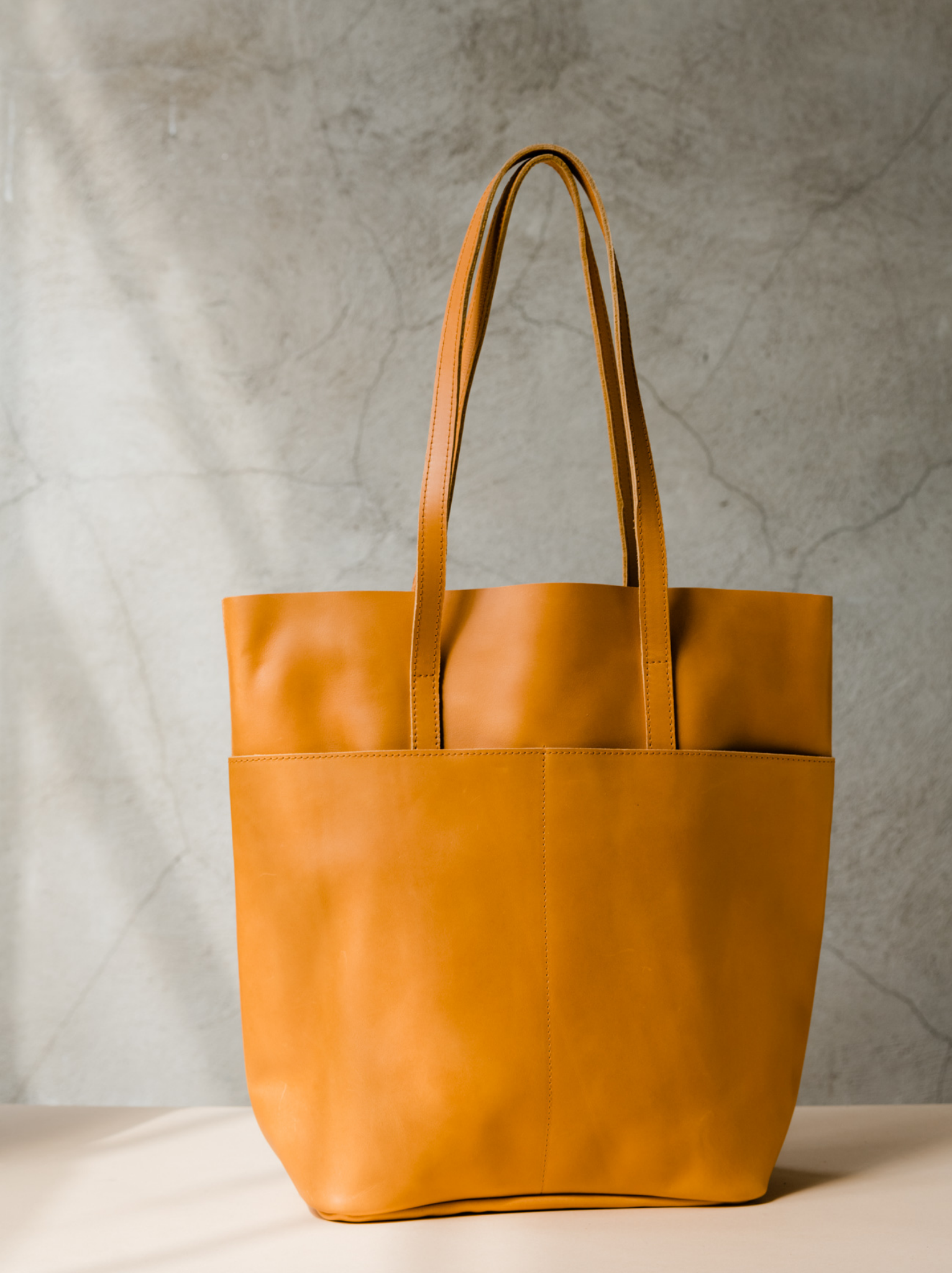 Orange cognac leather tote with shoulder straps and two slip pockets on a tan surface against a neutral background. #Color_Cognac