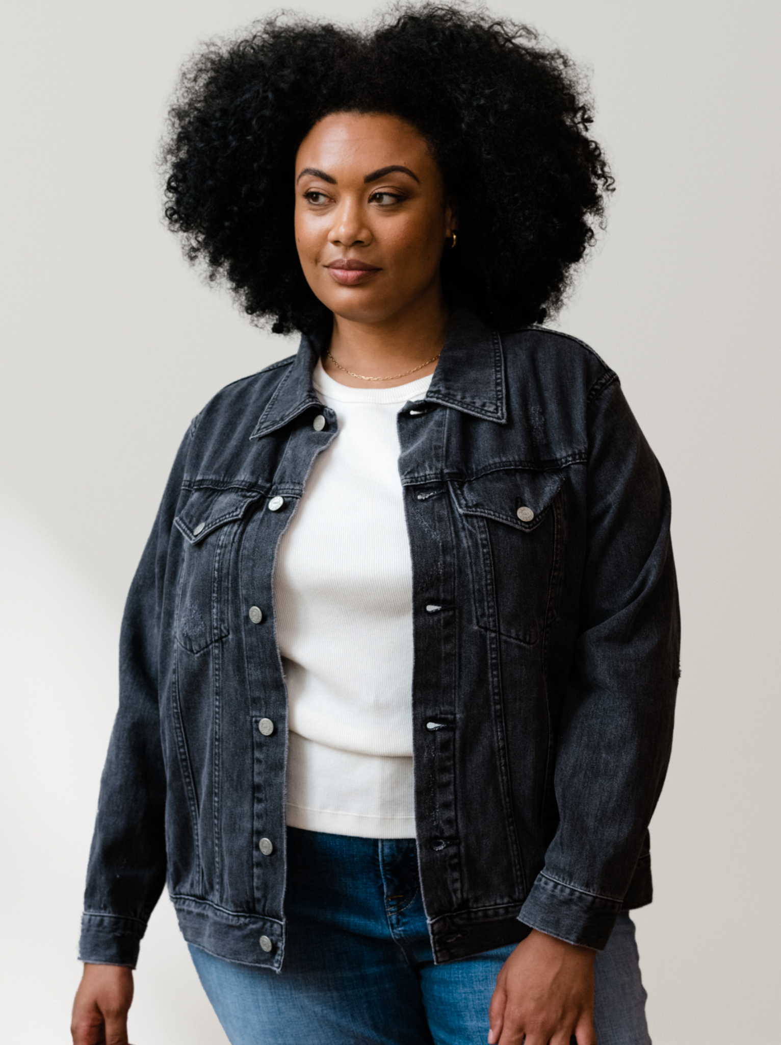 Woman wearing The Merly Jacket Washed Black over a white shirt and blue jeans on a plain background #Color_Washed Black