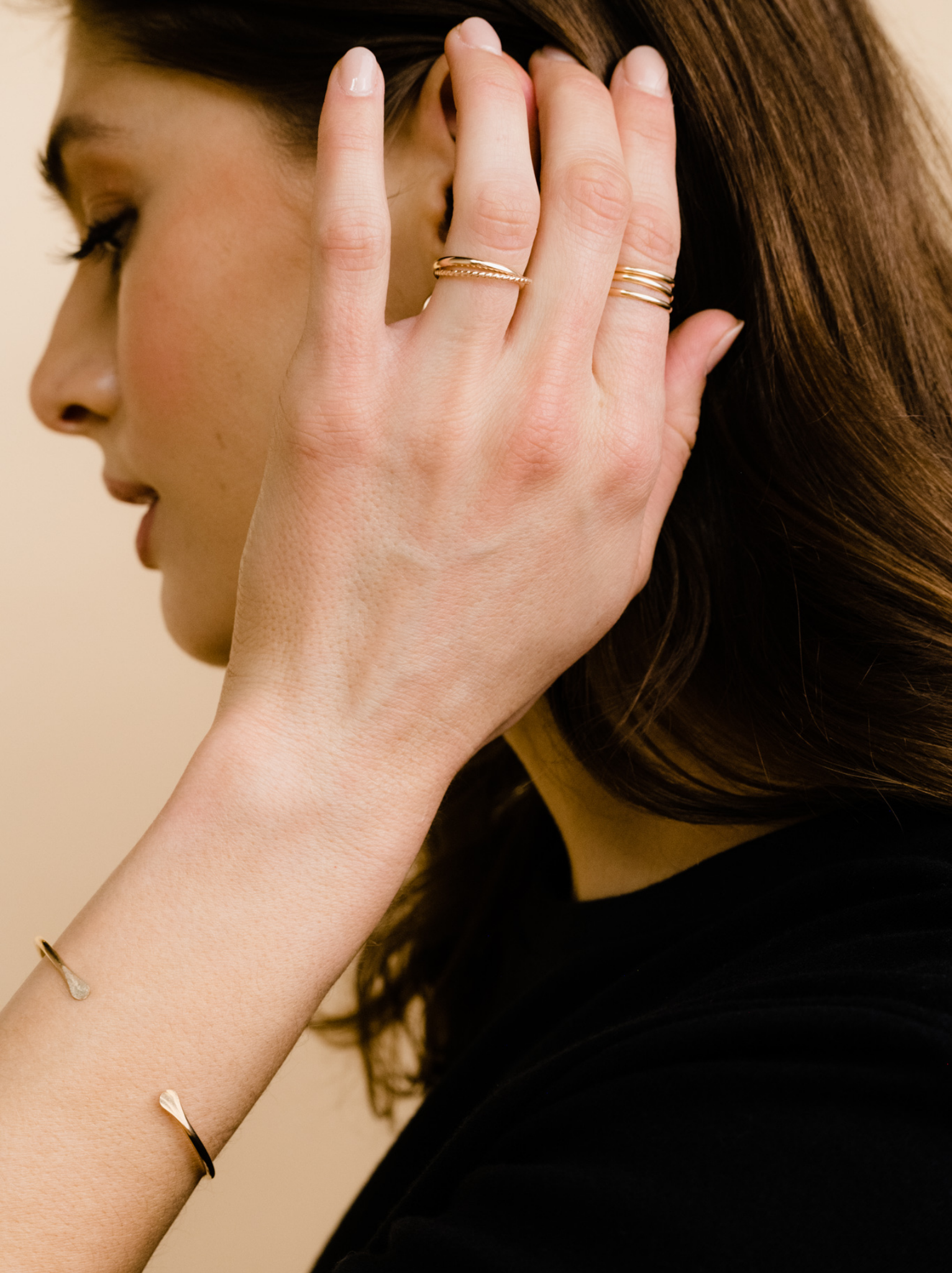 Close up of a woman wearing the two band interlocked gold ring and another ring, with a gold bracelet.