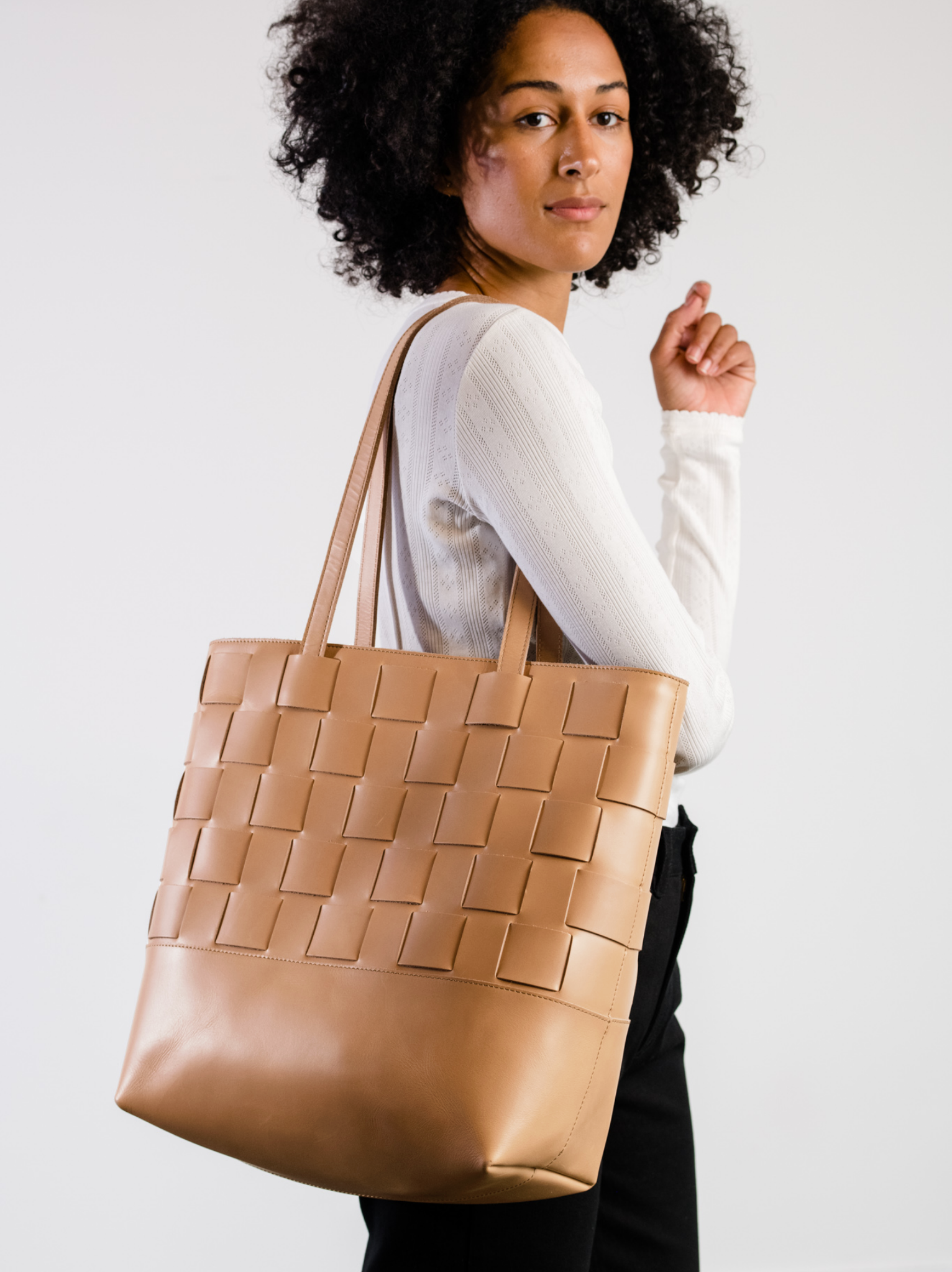 Woman with tan woven leather tote held as shoulder bag #Color_Mojave