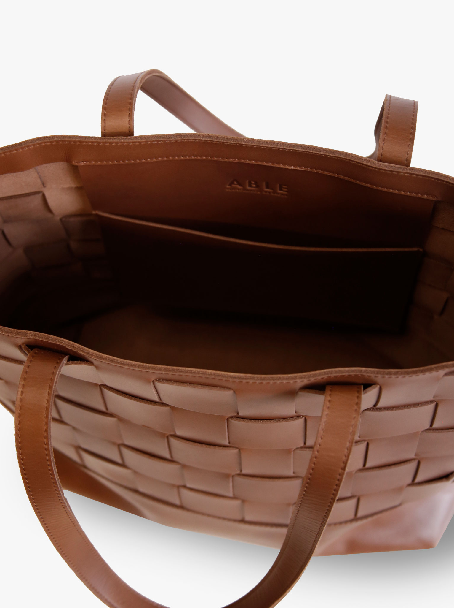 Interior slip pocket of brown woven leather tote. #Color_Whiskey