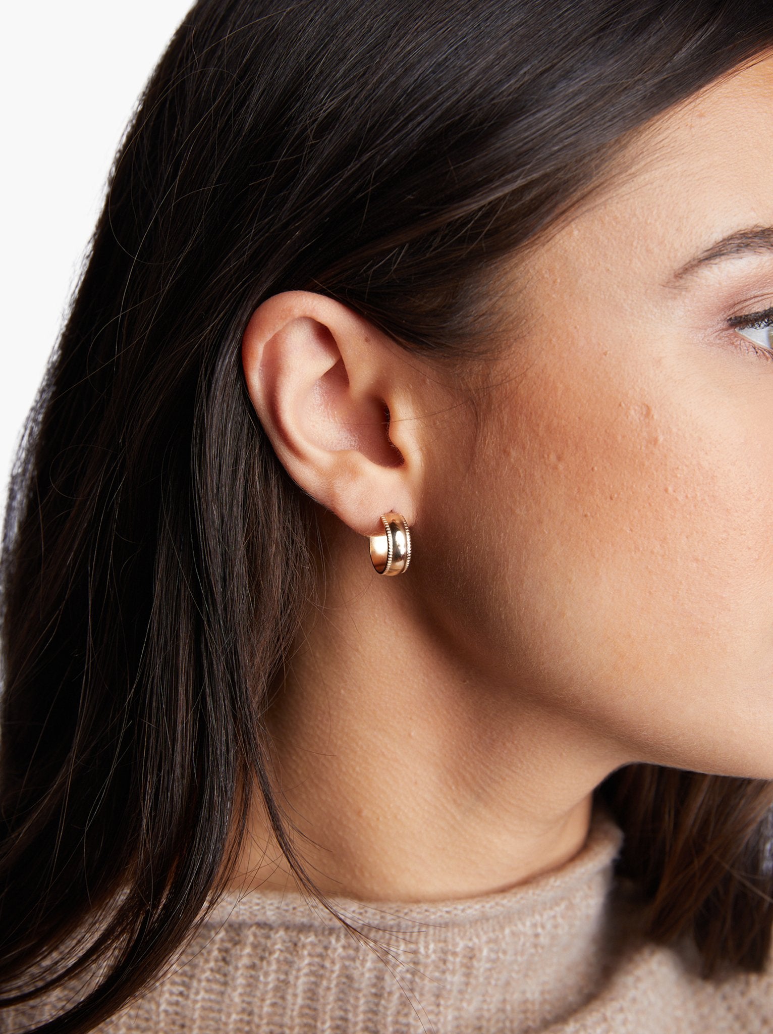A close up of a woman wearing a small gold hoop earring with a turtleneck sweater. #Color_14k Gold-filled