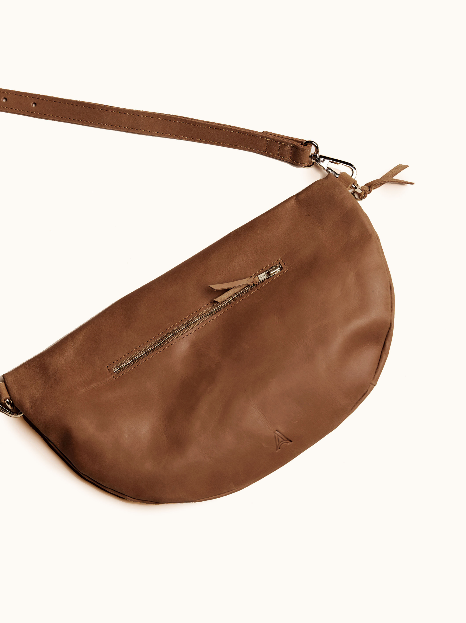 Back of brown leather belt bag with exterior zipper pocket with leather pull and brand mark on white background. #Color_Whiskey