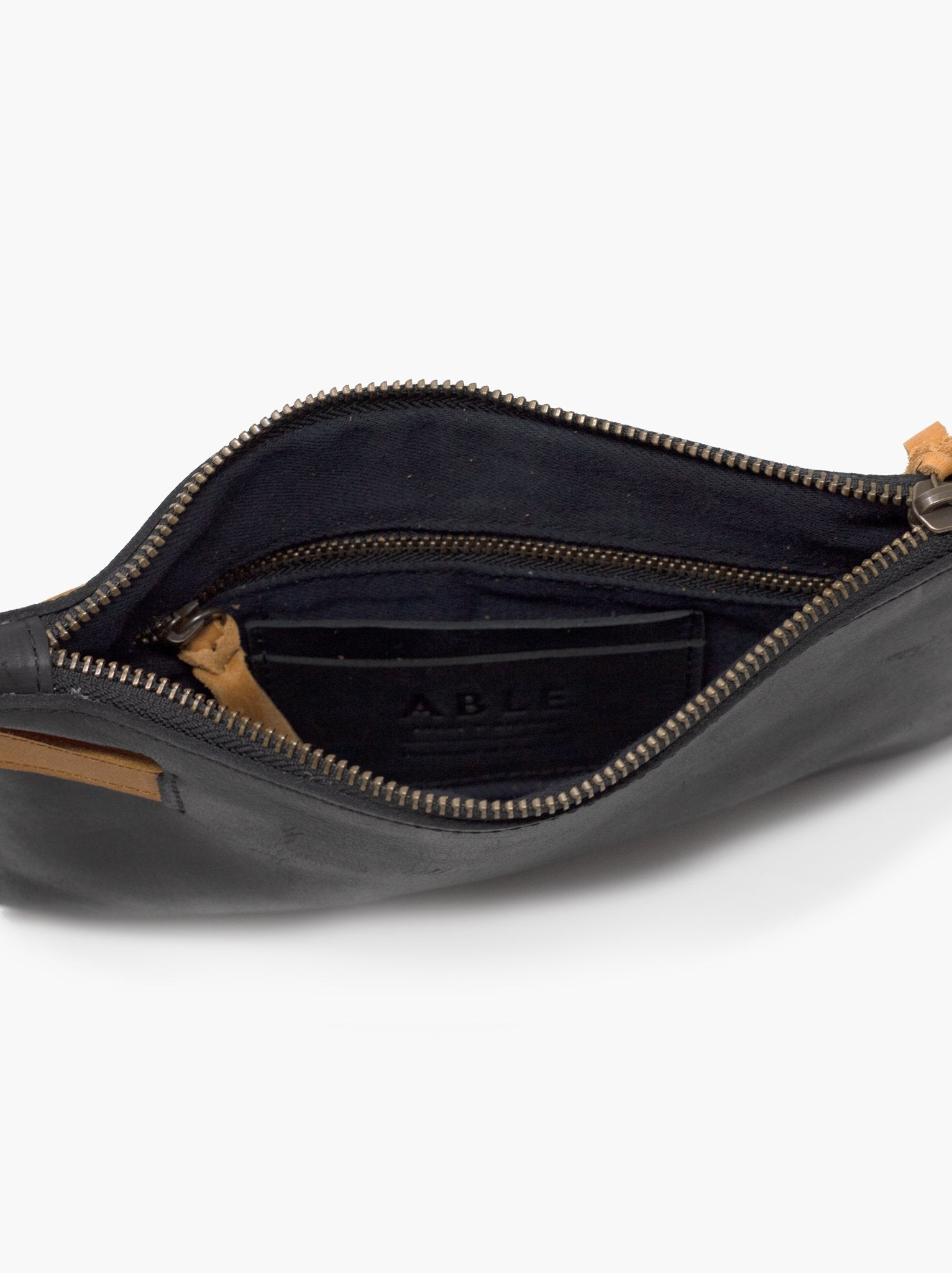 Lined interior of black and cognac leather wristlet with zipper pocket and card slots on white background. #Color_Black/Cognac