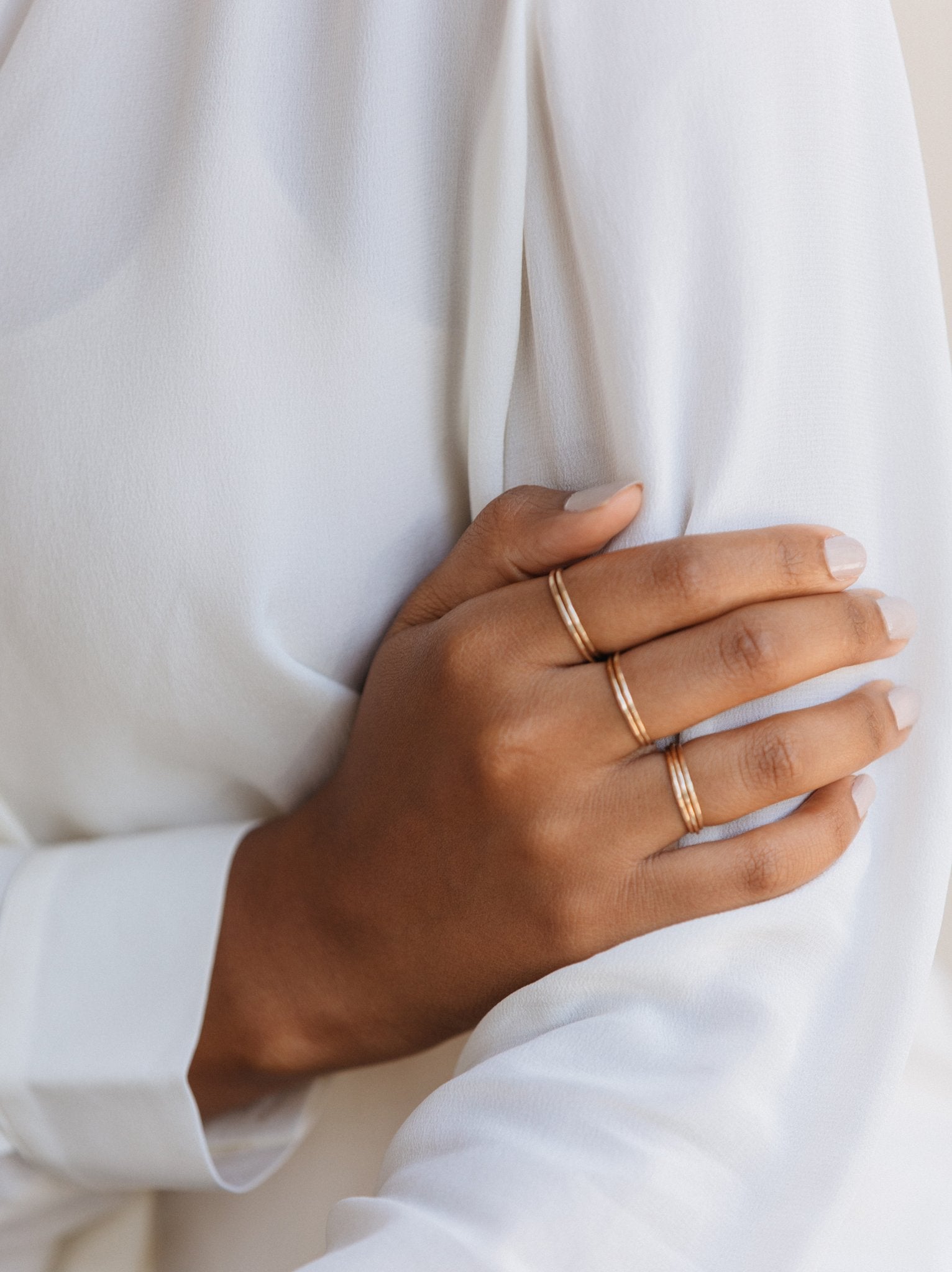 Close up of woman's hand wearing stacked gold hammered textured rings on three fingers.