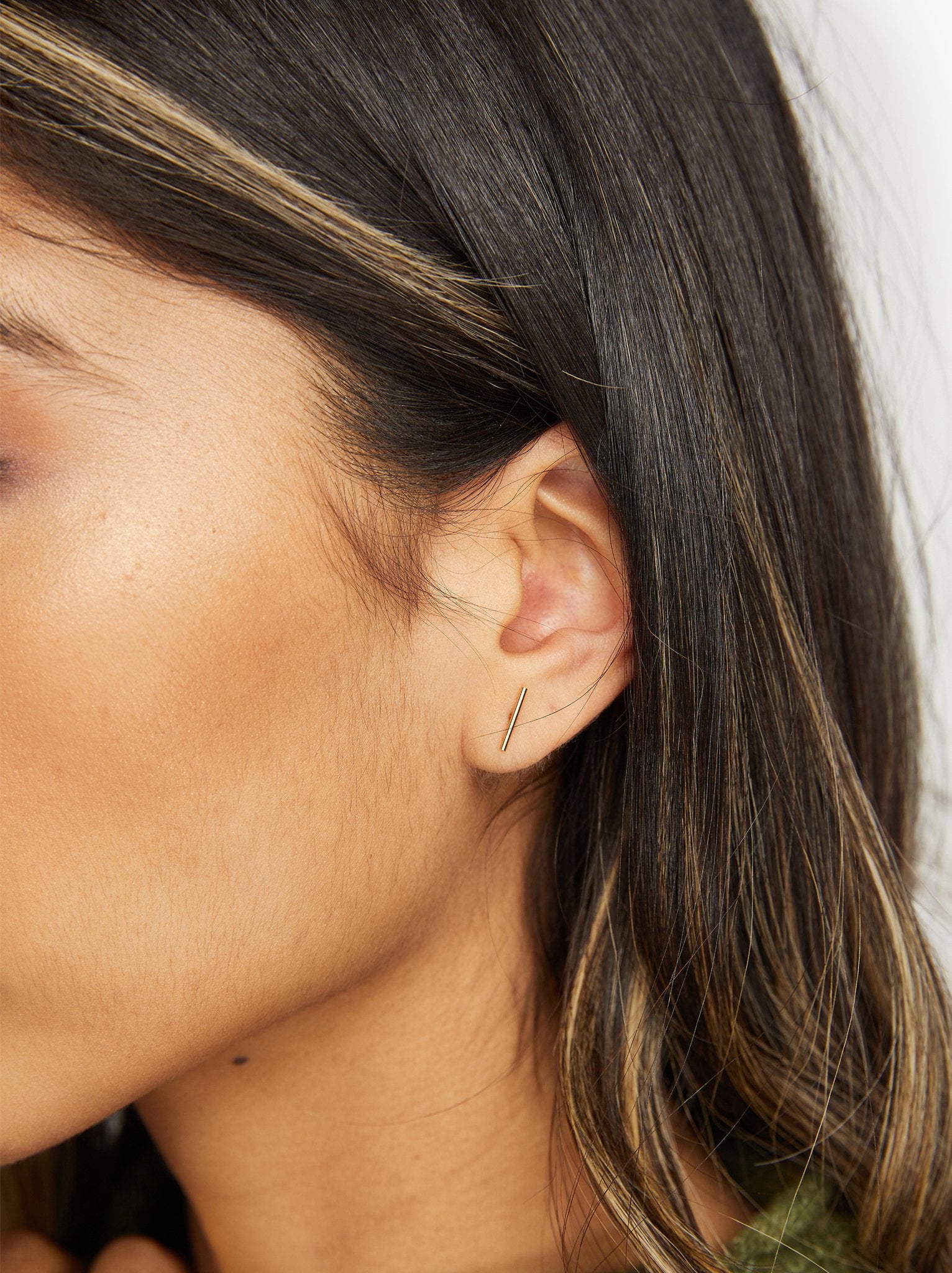 A close up of a woman wearing a gold stick stud earring. #Color_14k Gold-filled