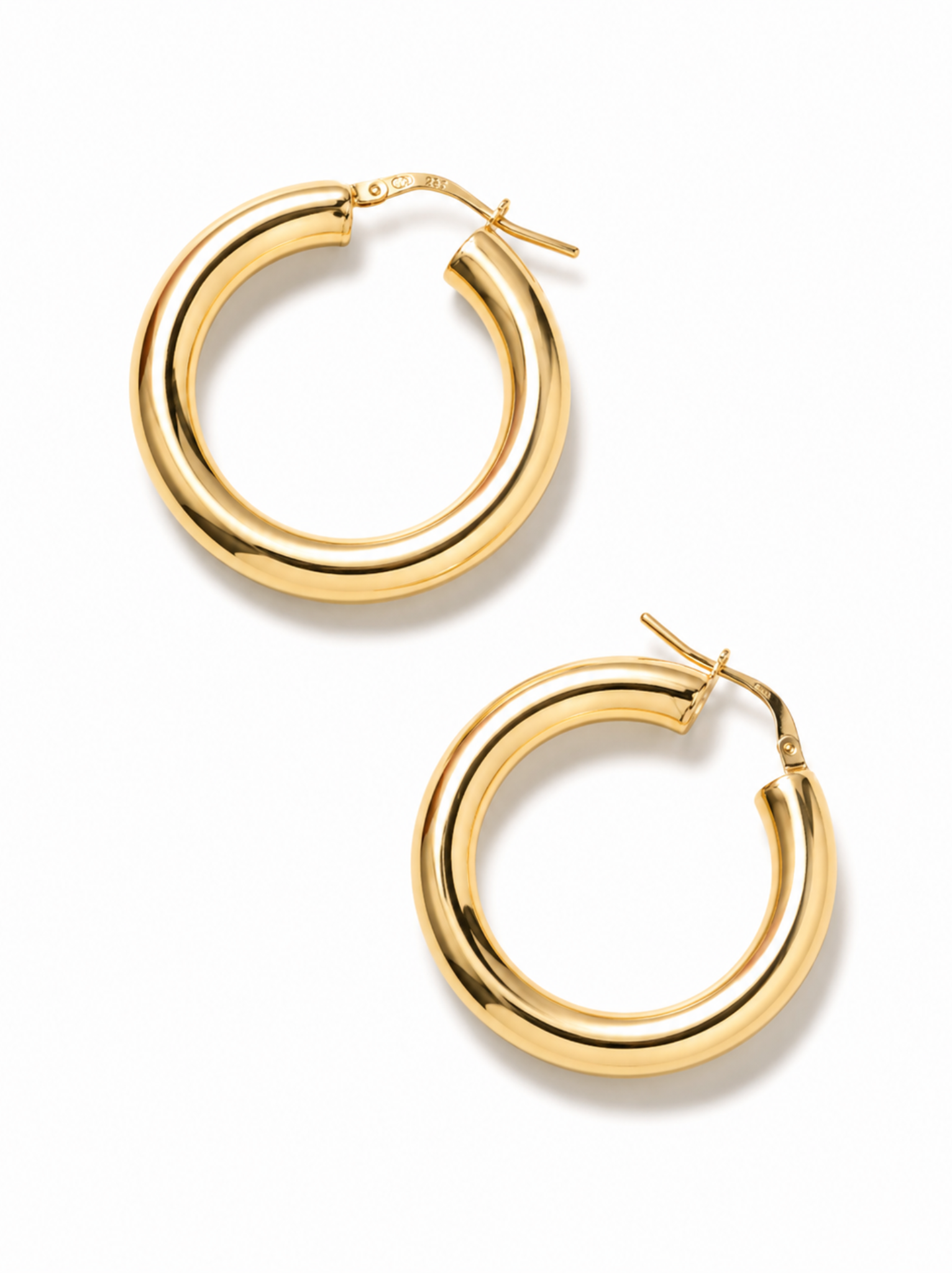 A pair of thick, polished gold hoop earrings with a classic latch back closure, displayed on a clean white background.