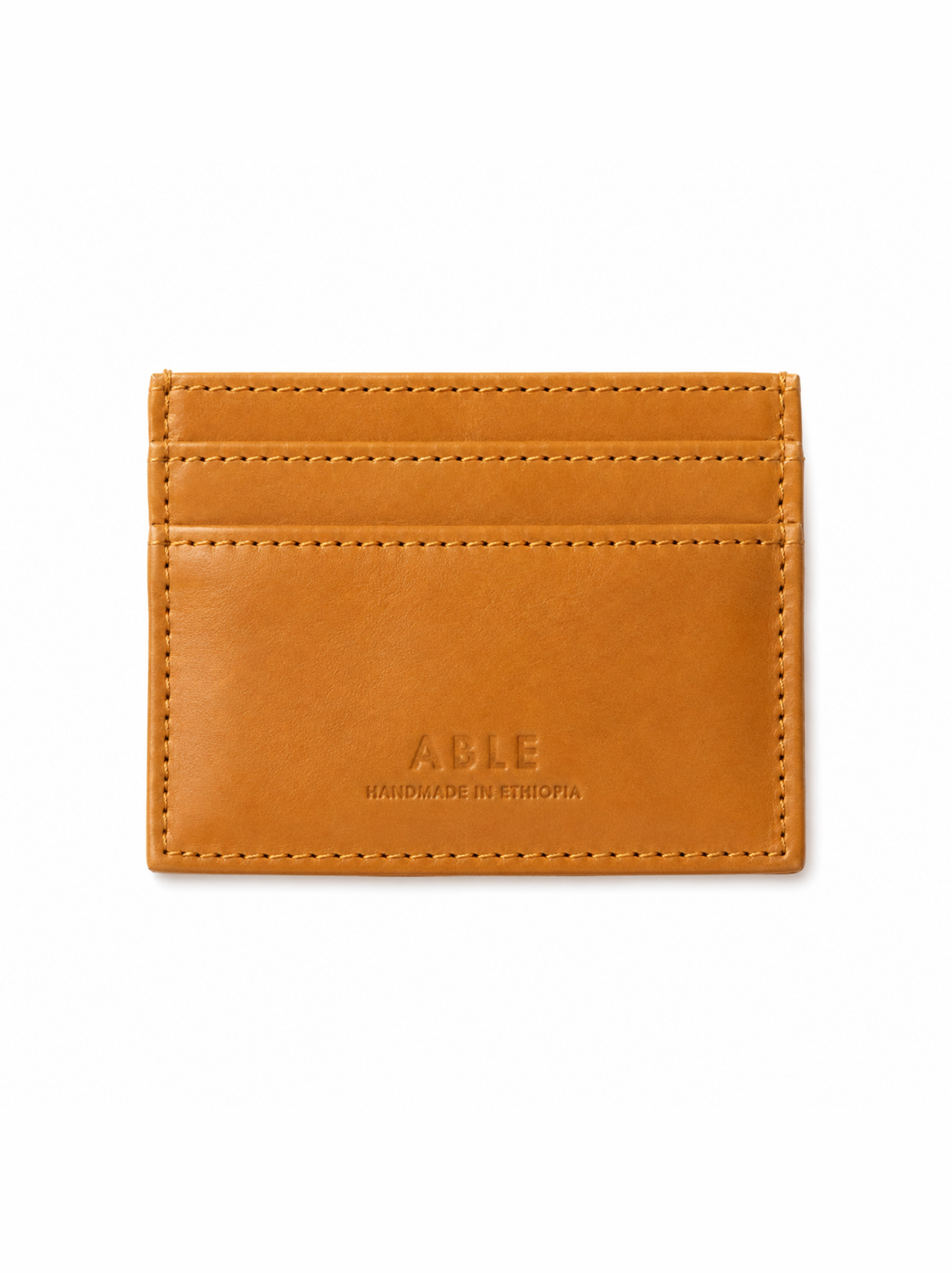 A slim, minimalist card holder wallet in cognac leather with double rows of stitching and debossed branding on the front, shown on a plain white background. #Color_Cognac