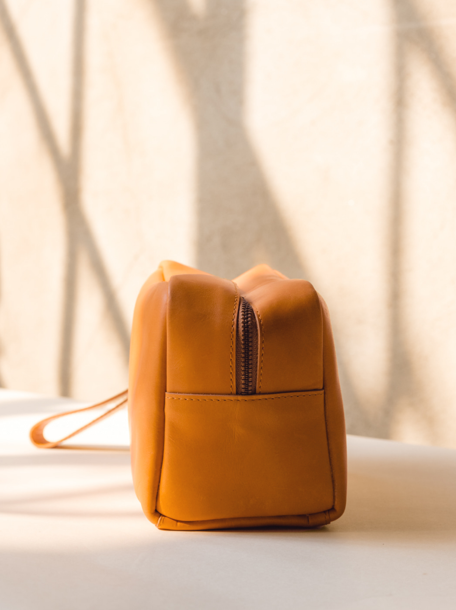 Zipper detail of cognac leather dopp kit on light background. #Color_Cognac