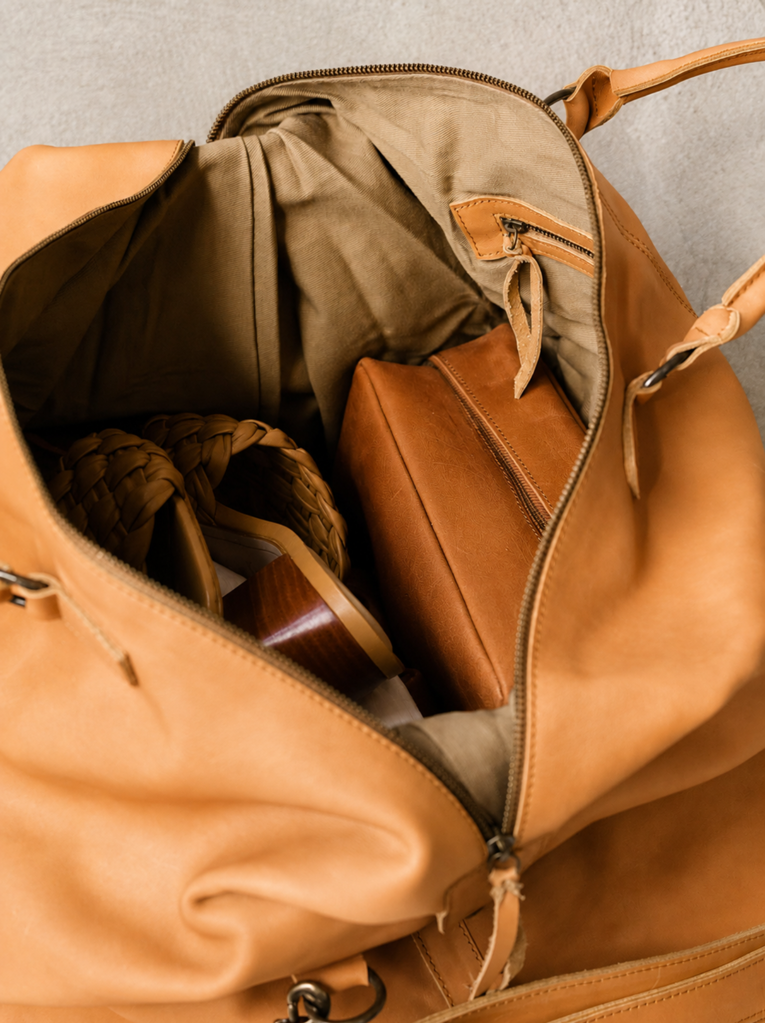 Close up of the interior of the cognac weekender with interior zipper pocket, a dopp kit and shoes. #Color_Cognac
