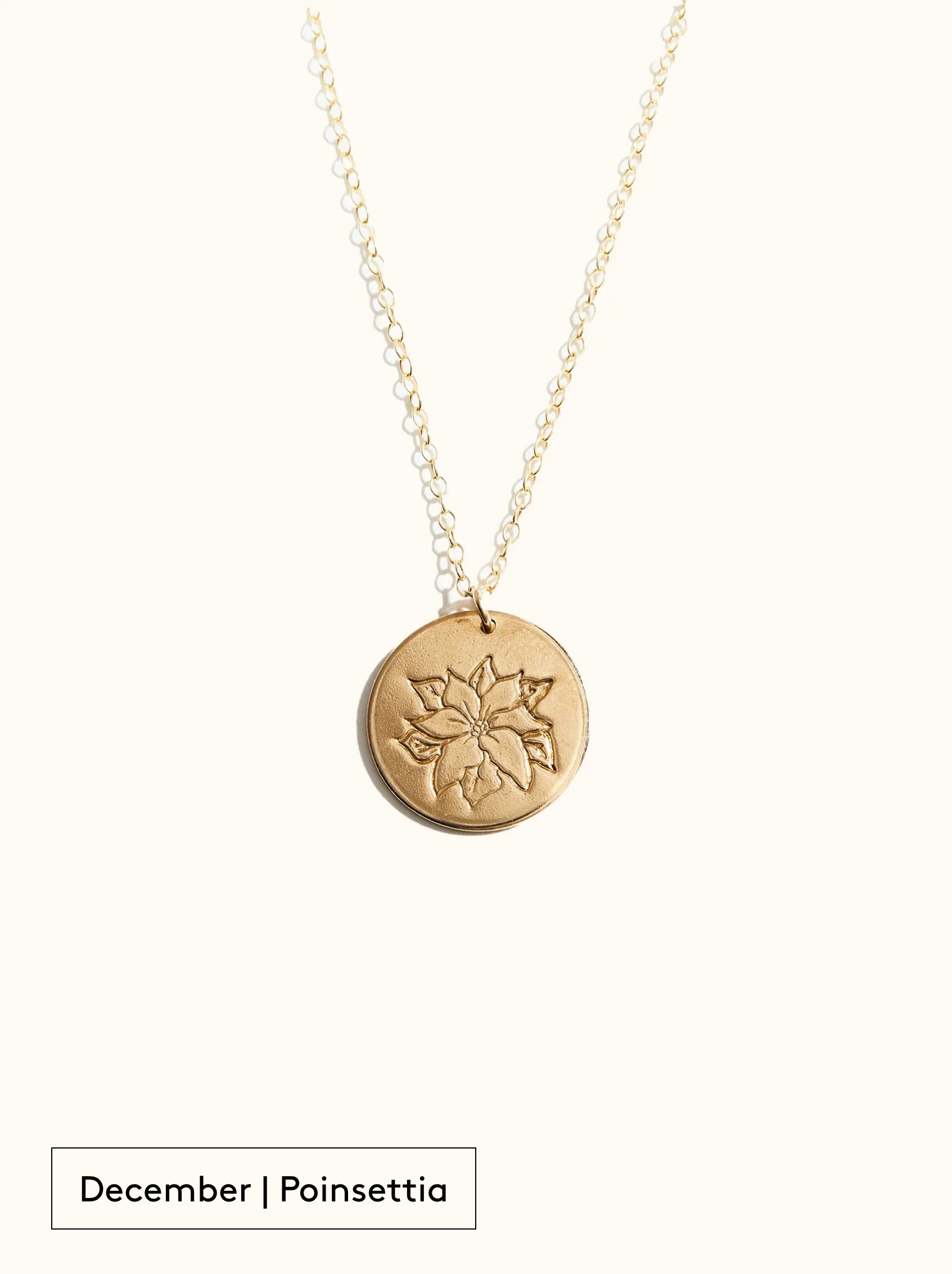 A gold-filled necklace with a round tag pendant featuring an engraved Poinsettia, noted as December's birth month flower, attached to a 24 inch chain on a neutral background.
