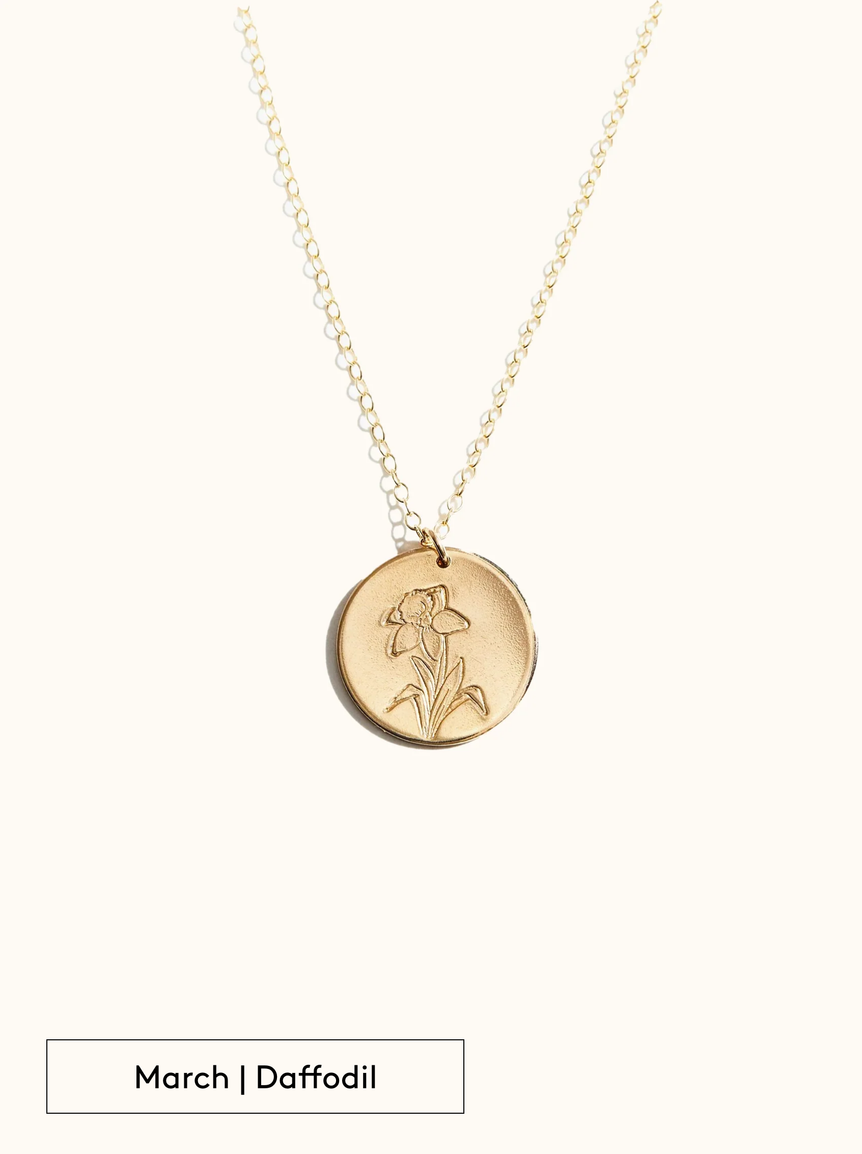 A gold-filled necklace with a round tag pendant featuring an engraved Daffodil, noted as March's birth month flower, attached to a 24 inch chain on a neutral background.
