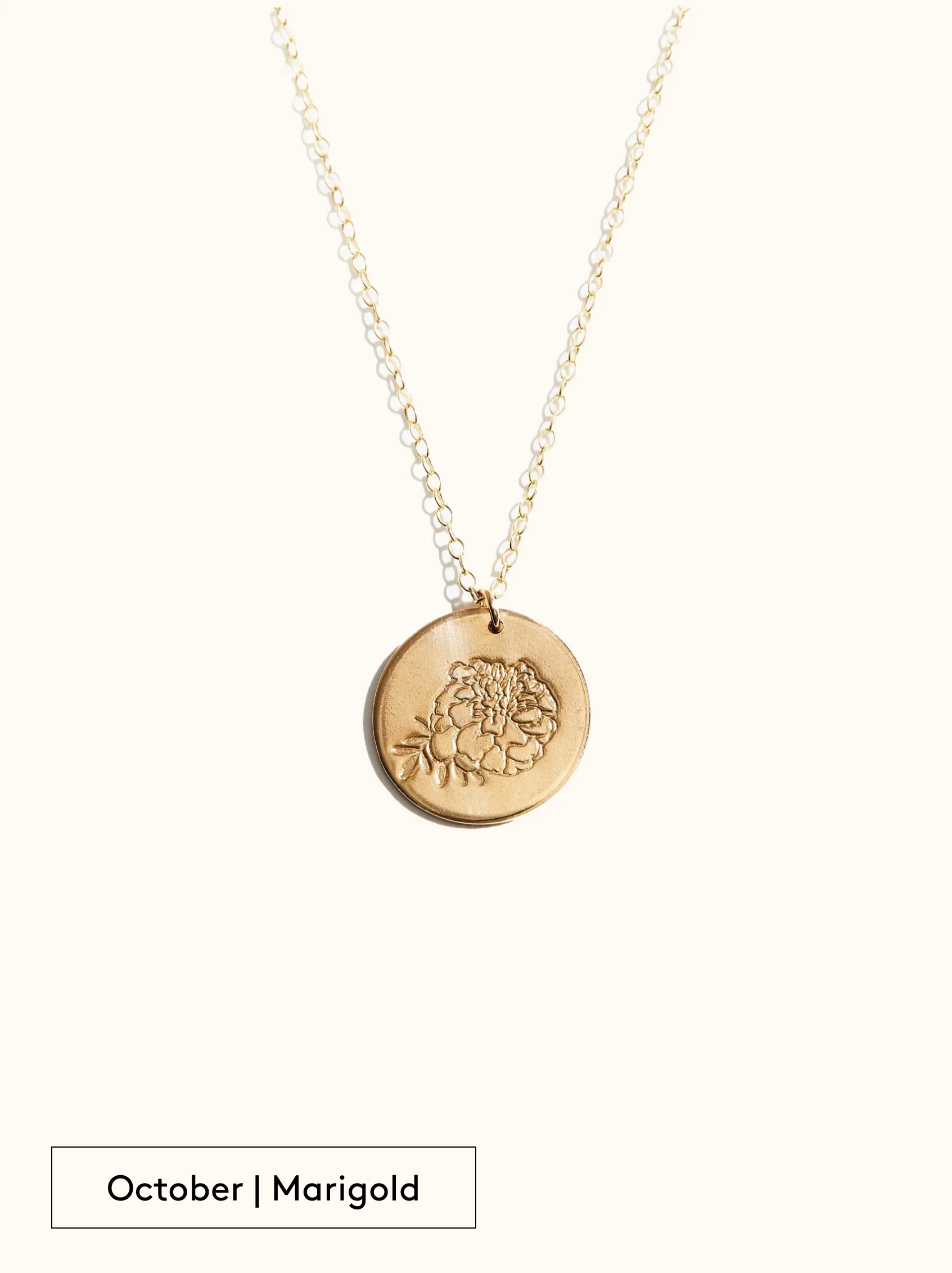 A gold-filled necklace with a round tag pendant featuring an engraved Marigold, noted as October's birth month flower, attached to a 24 inch chain on a neutral background.