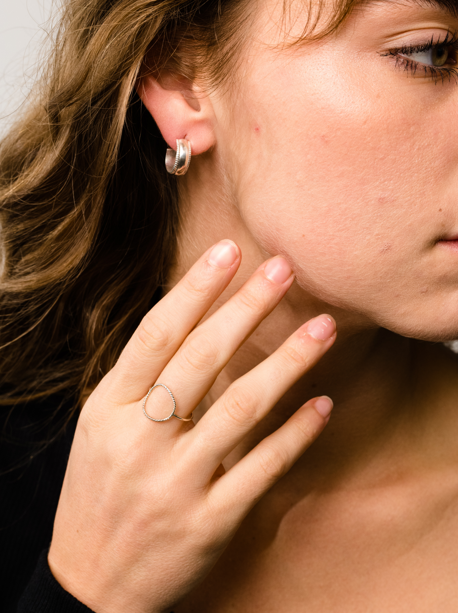 Close-up of a woman wearing a small silver hoop earring and a silver circle ring on her finger. #Color_Sterling SIlver