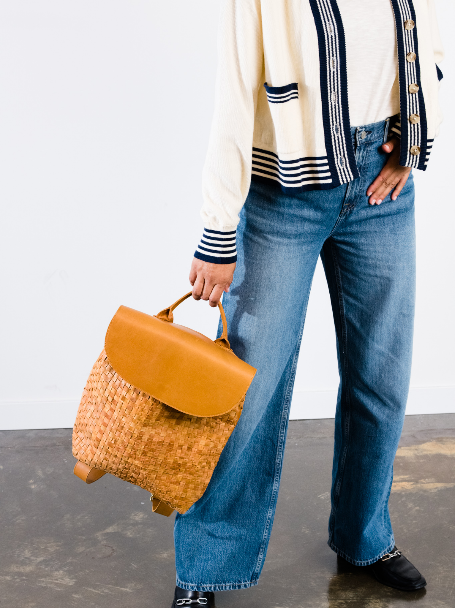 Woman holding orange basketweave backpack by its top handle. #Color_Cognac