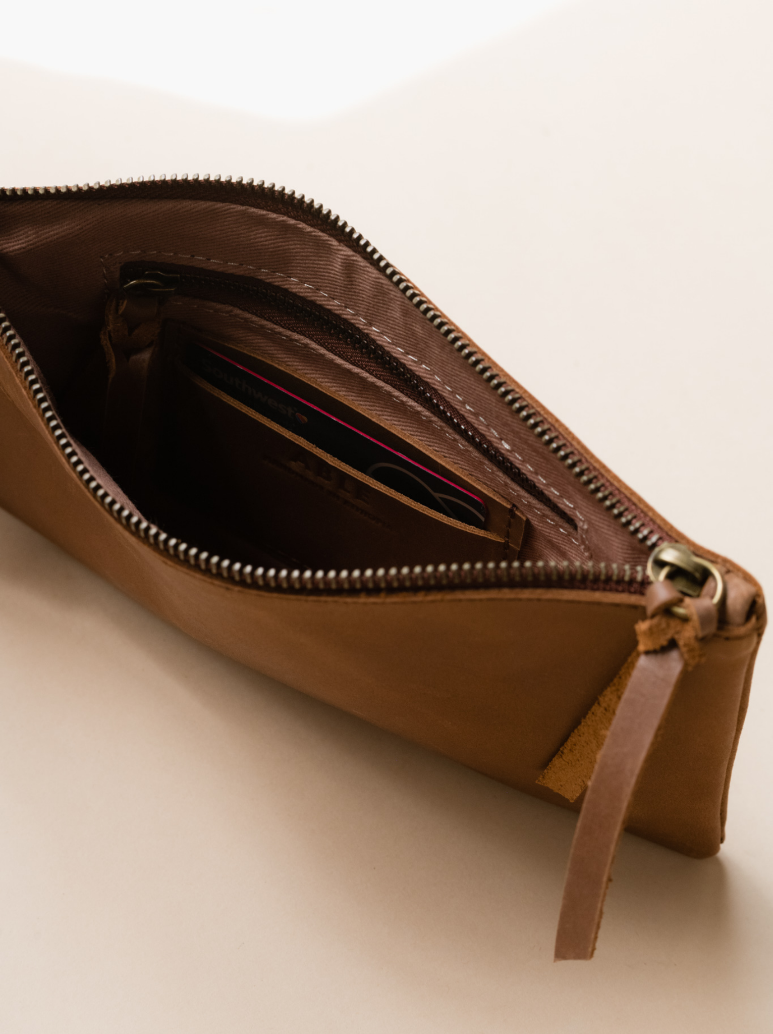 Lined interior of brown leather wristlet with zipper pocket and card slots on neutral background. #Color_Whiskey