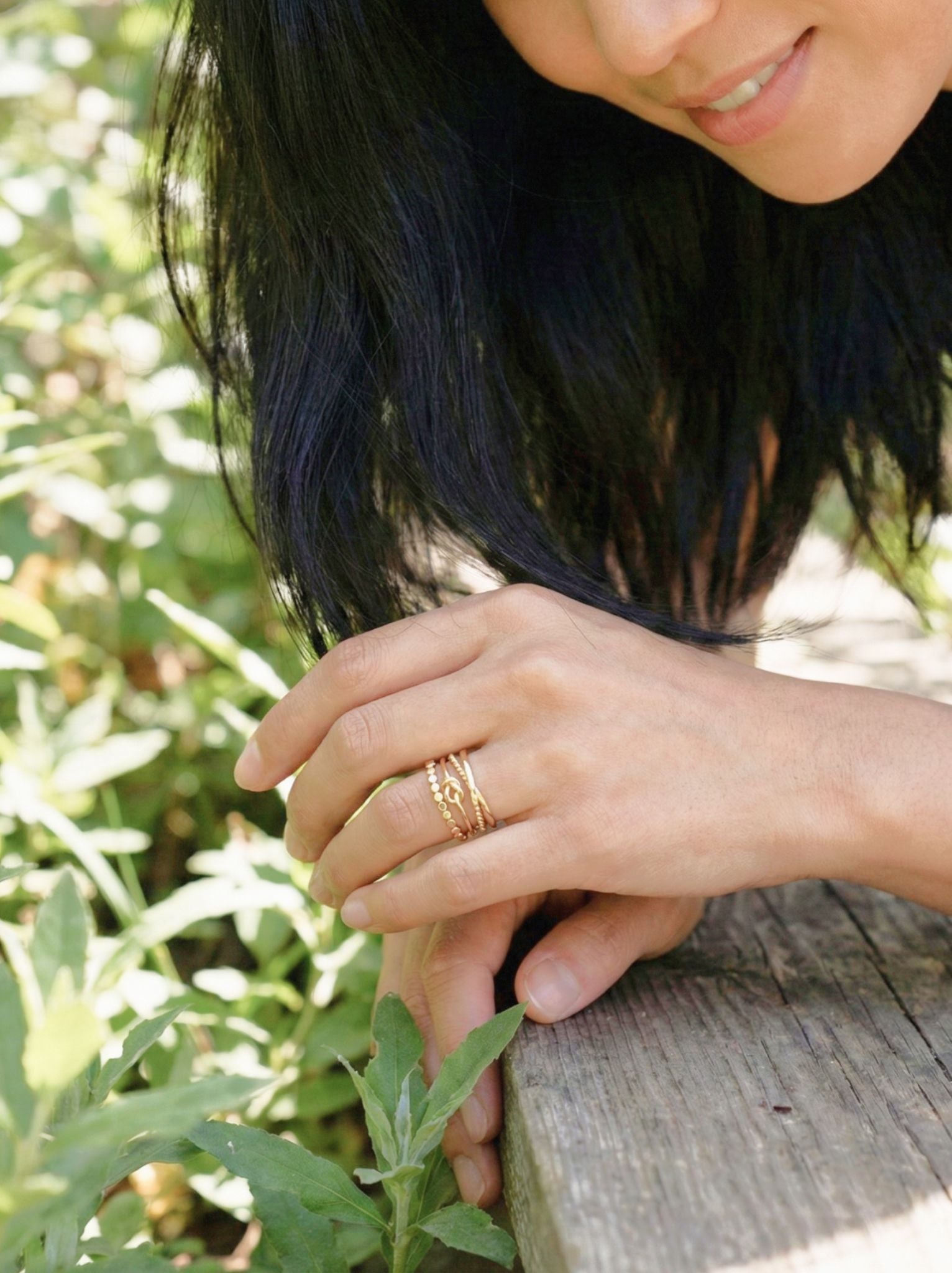 Woman with a gold ring on her finger sitting outdoors among greenery