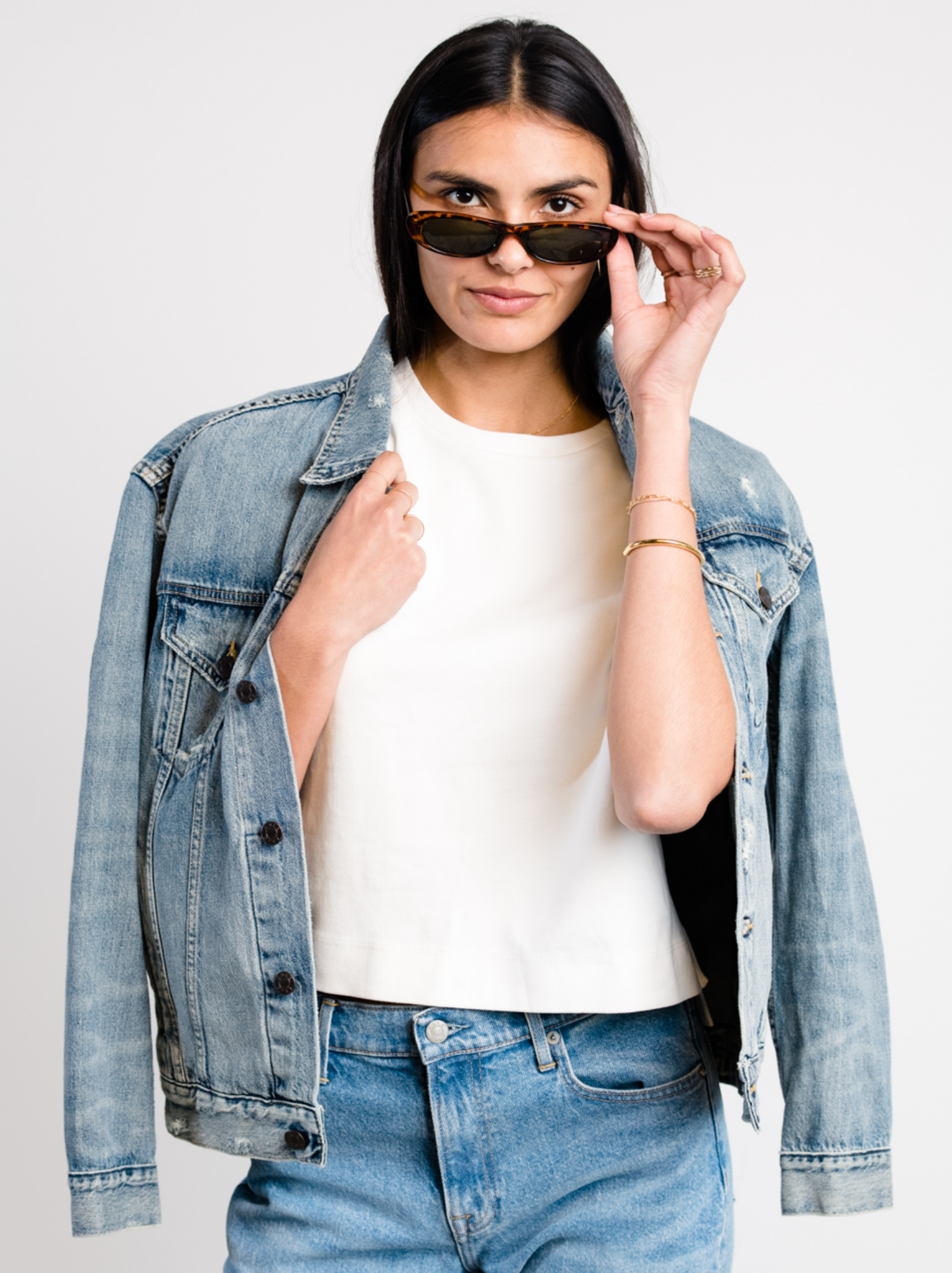 Woman wearing light blue denim jacket with light distressing, white shirt, and sunglasses against a white background. #Color_Original Wash