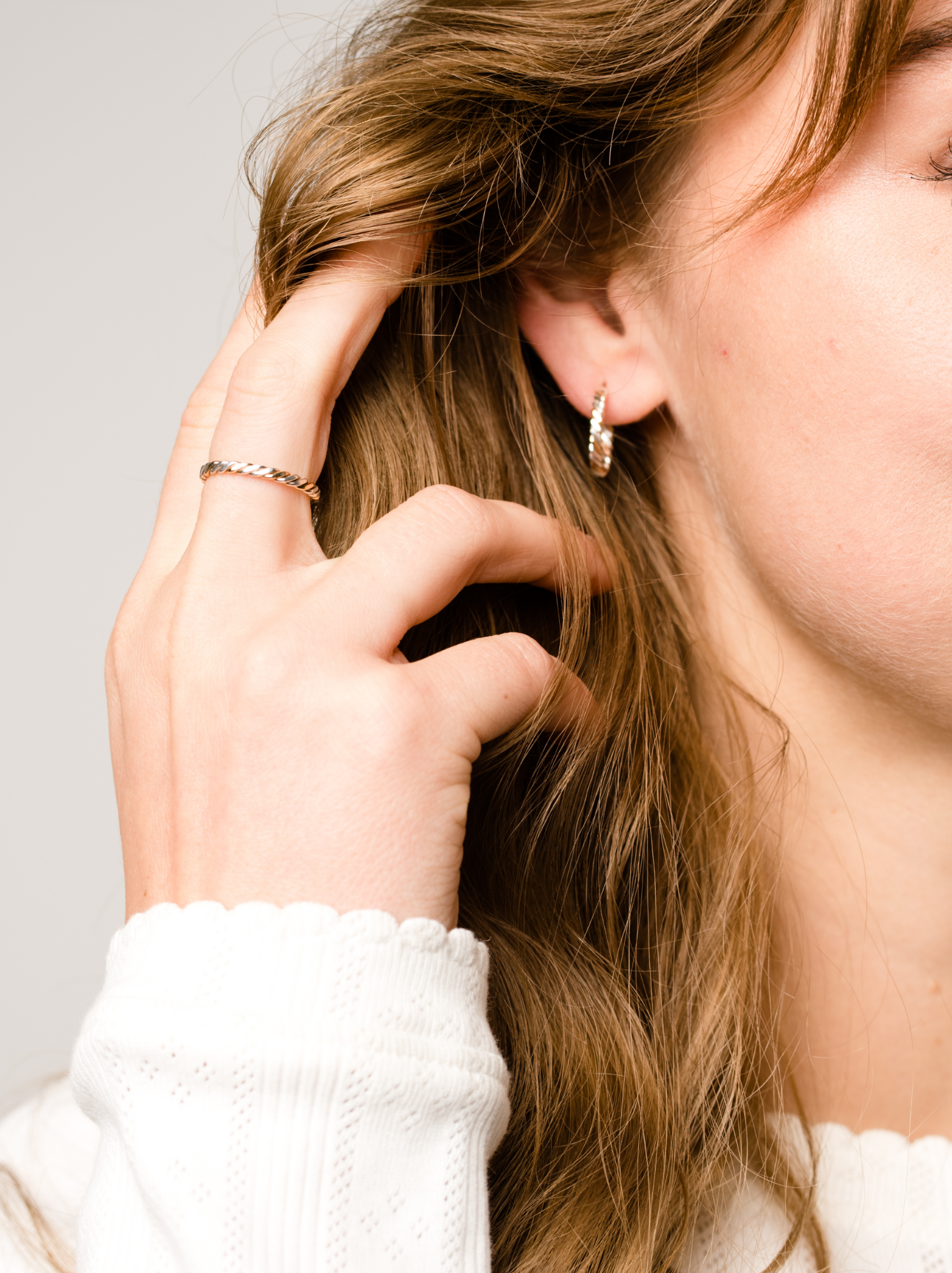 Close up of a woman wearing a two-tone gold and silver twisted ring with matching earring.
