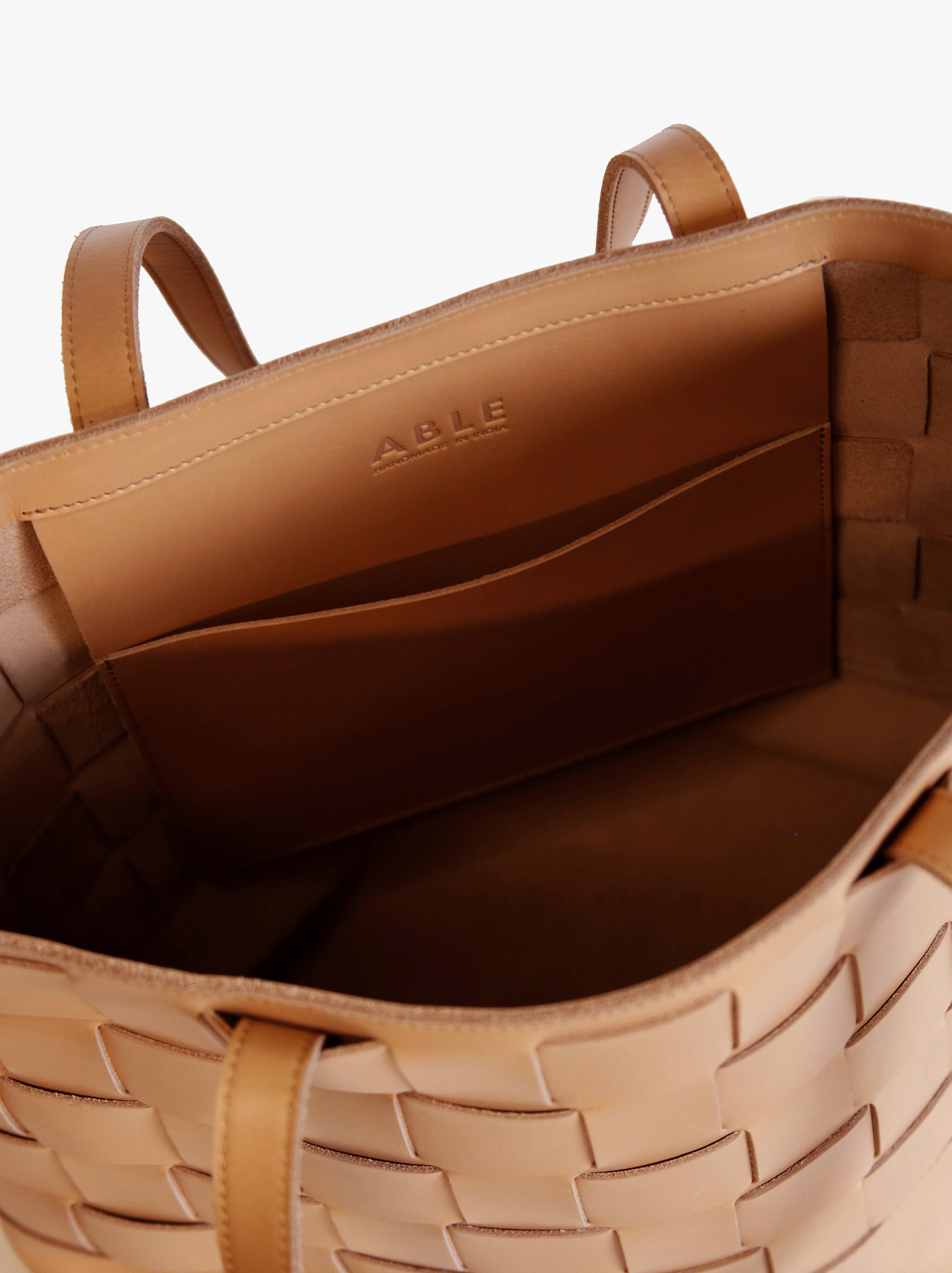 Interior slip pocket of tan leather woven tote against white background #Color_Mojave