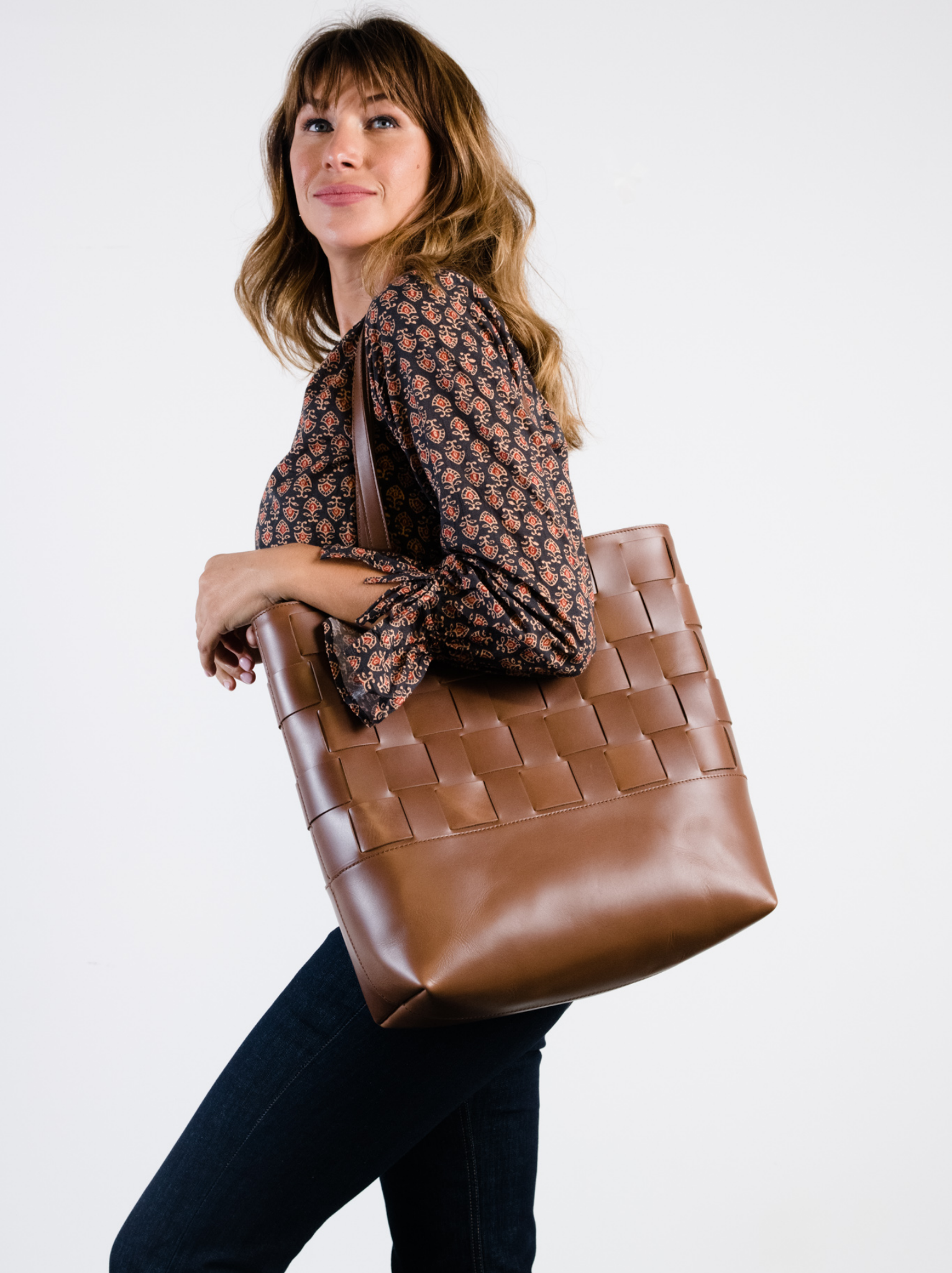 Women with brown leather woven tote being held as shoulder bag. #Color_Whiskey