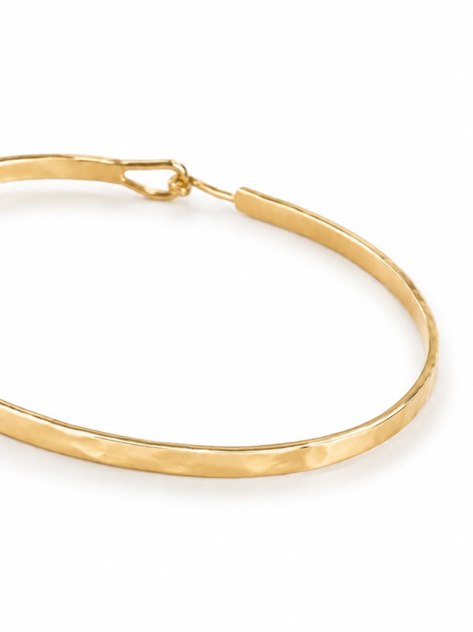 Close up shot shot showing hammered detailed of gold bangle with hook-and-eye closure on a white background.