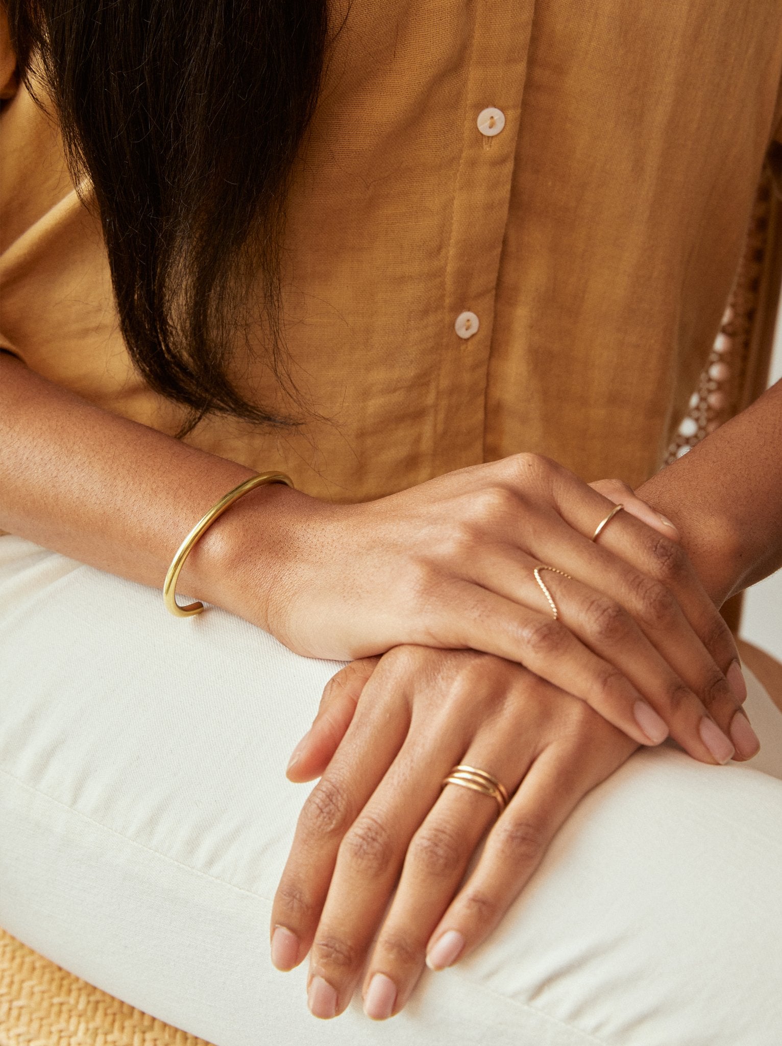 Close up of woman wearing a gold cuff bracelet on her wrist with rings on her fingers.