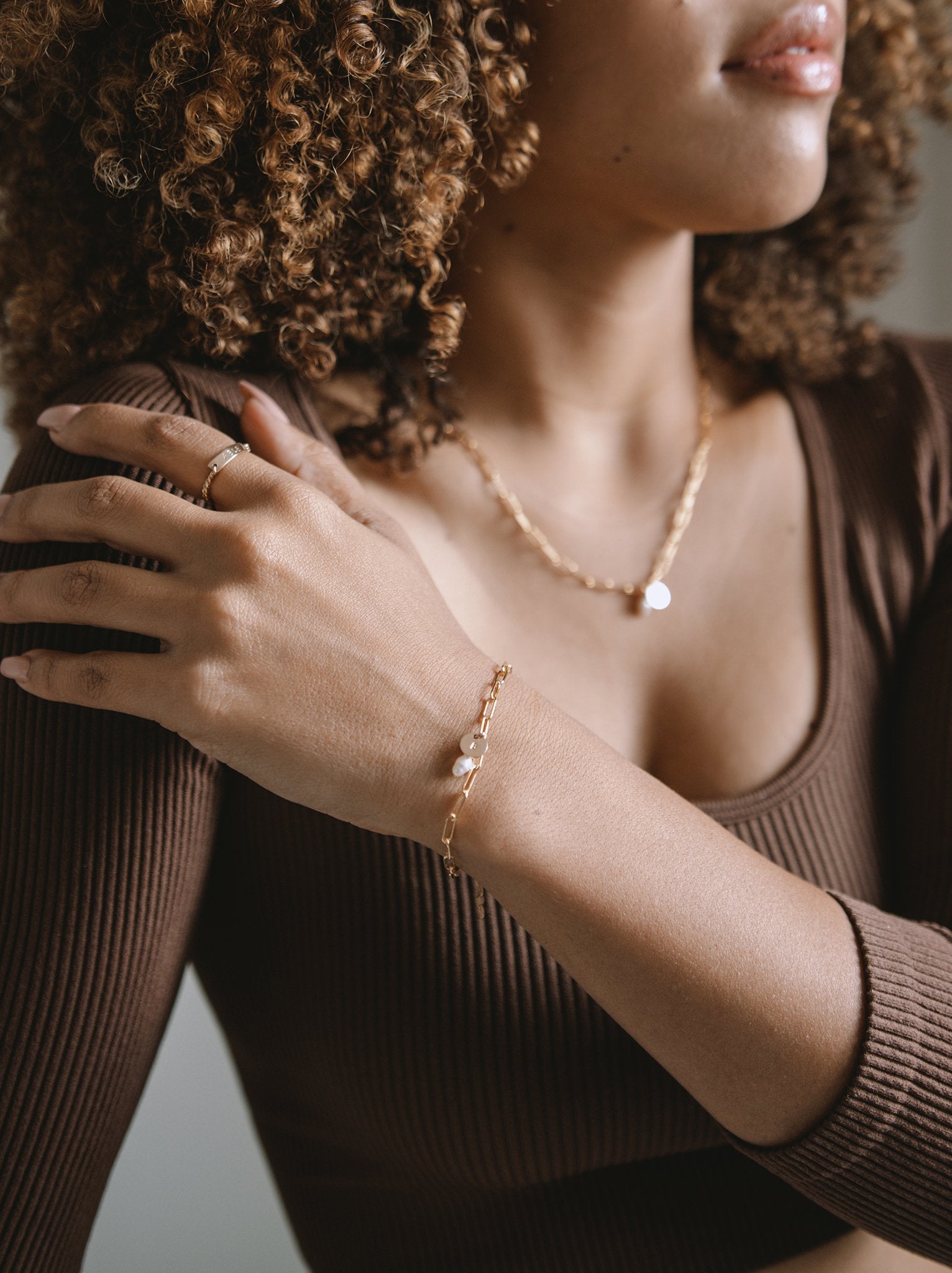 Close up of a woman wearing gold bracelet with pearl and pendant add ons on her wrist with matching necklace.